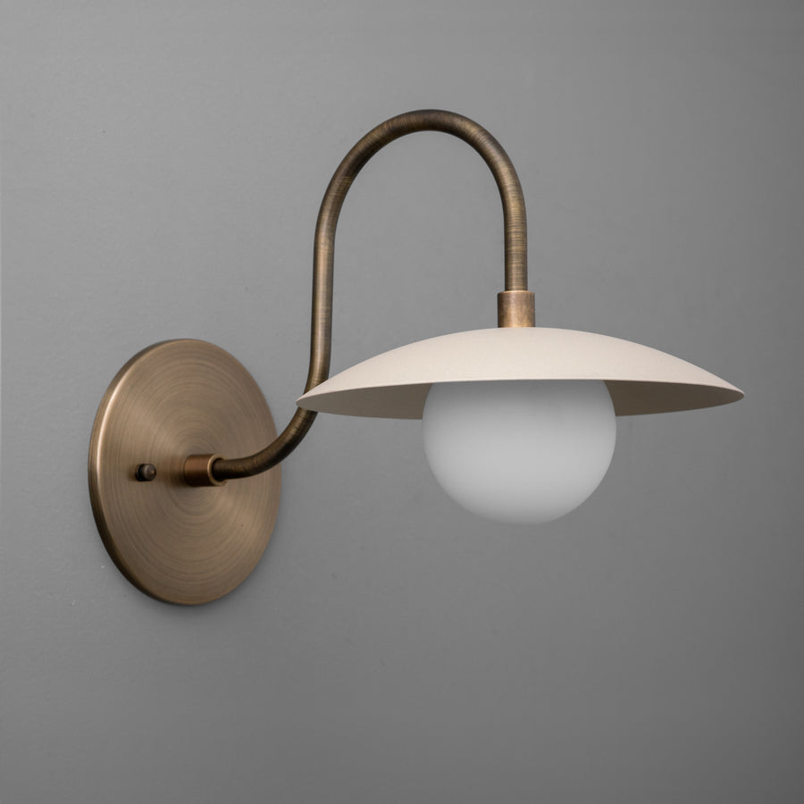 Wall sconce with antique brass curved arm, cream metal shade, and frosted globe bulb. - SCONCE MODEL NO. 3799