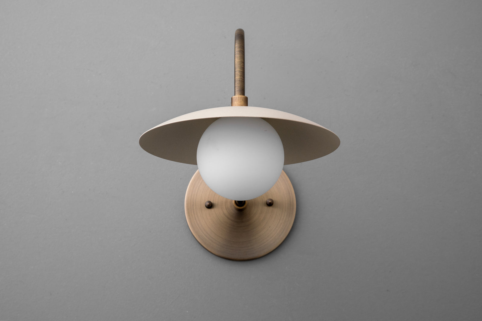 Antique brass wall sconce with cream dome shade and frosted globe bulb on gray background. - SCONCE MODEL NO. 3799