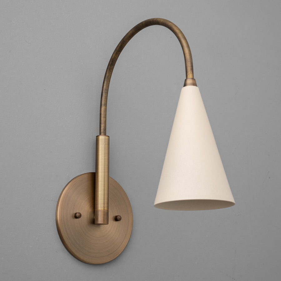 Antique brass wall sconce with a curved arm and cream conical shade against a gray background. - SCONCE MODEL NO. 1309