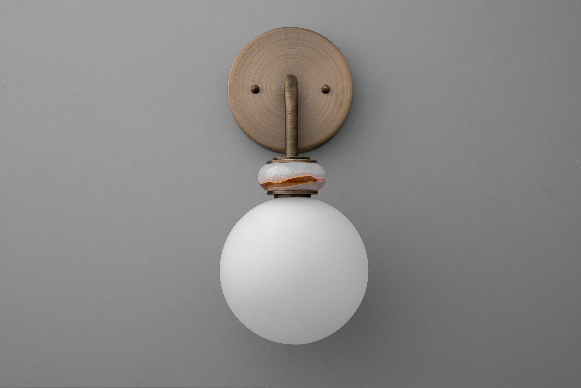 Wall sconce with matte white glass globe and antique brass circular backplate on gray wall. - SCONCE MODEL NO. 5448
