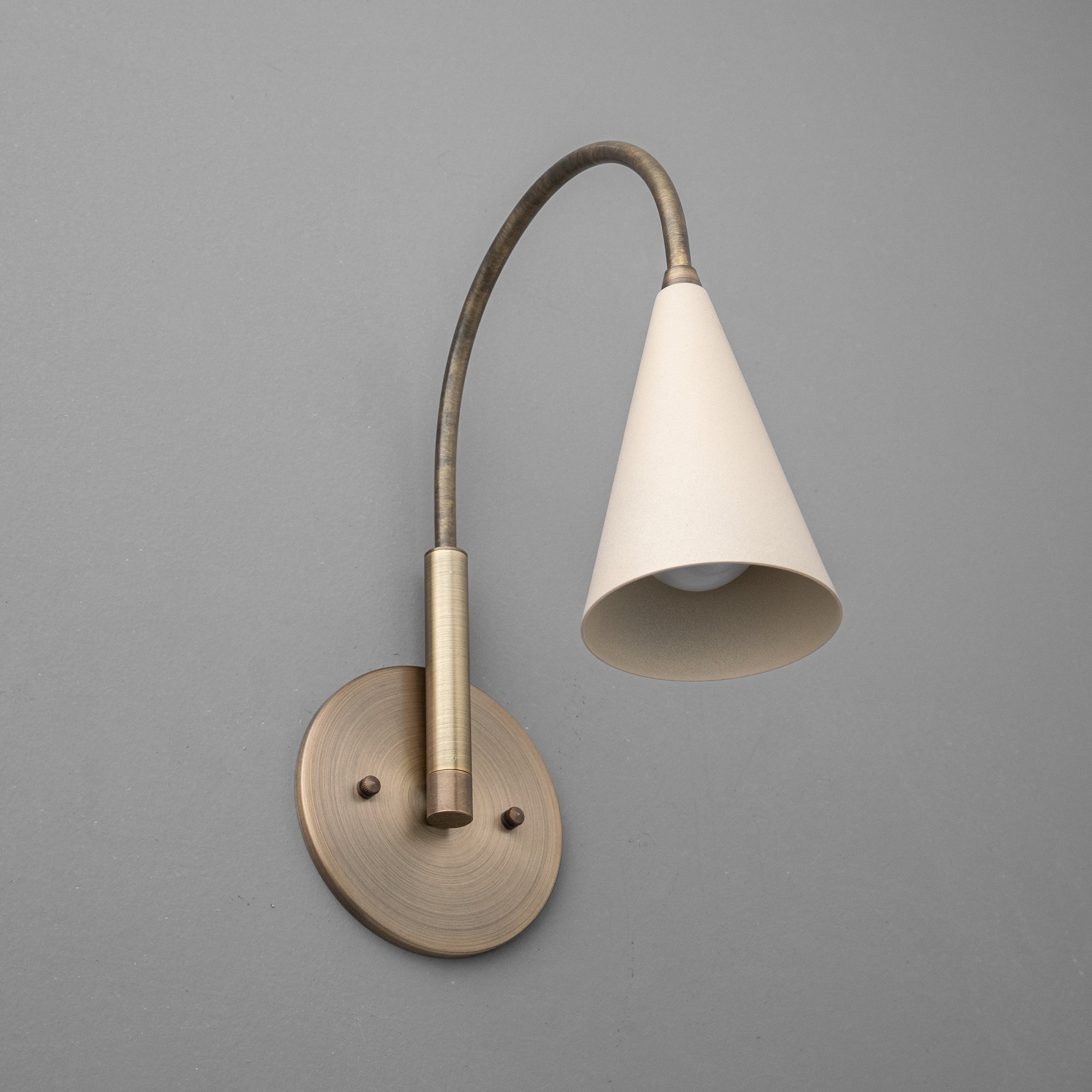 Antique brass wall sconce with curved arm and cream conical shade against gray background. - SCONCE MODEL NO. 1309