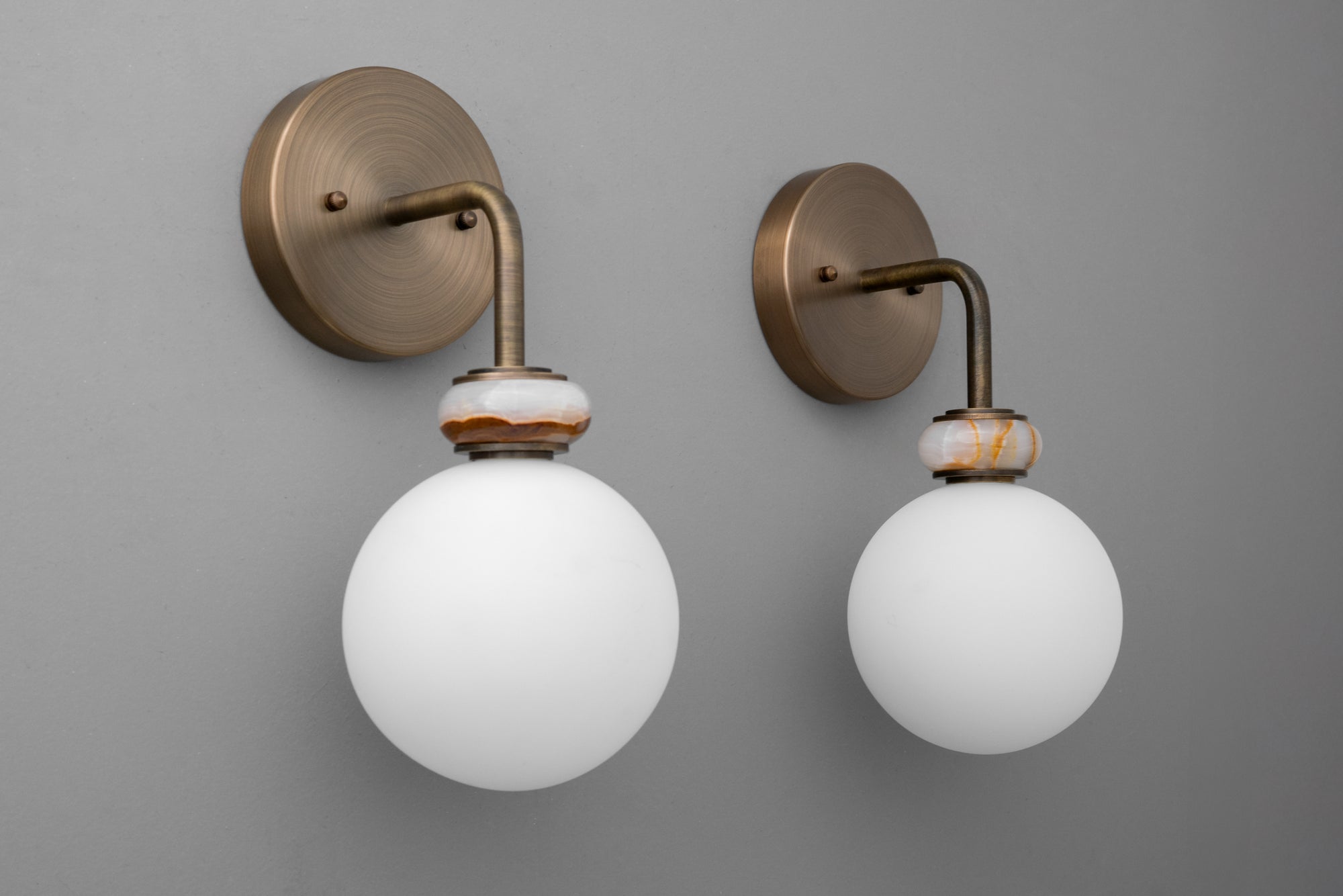 Pair of antique brass wall sconces with white frosted glass globes on gray background. - SCONCE MODEL NO. 5448