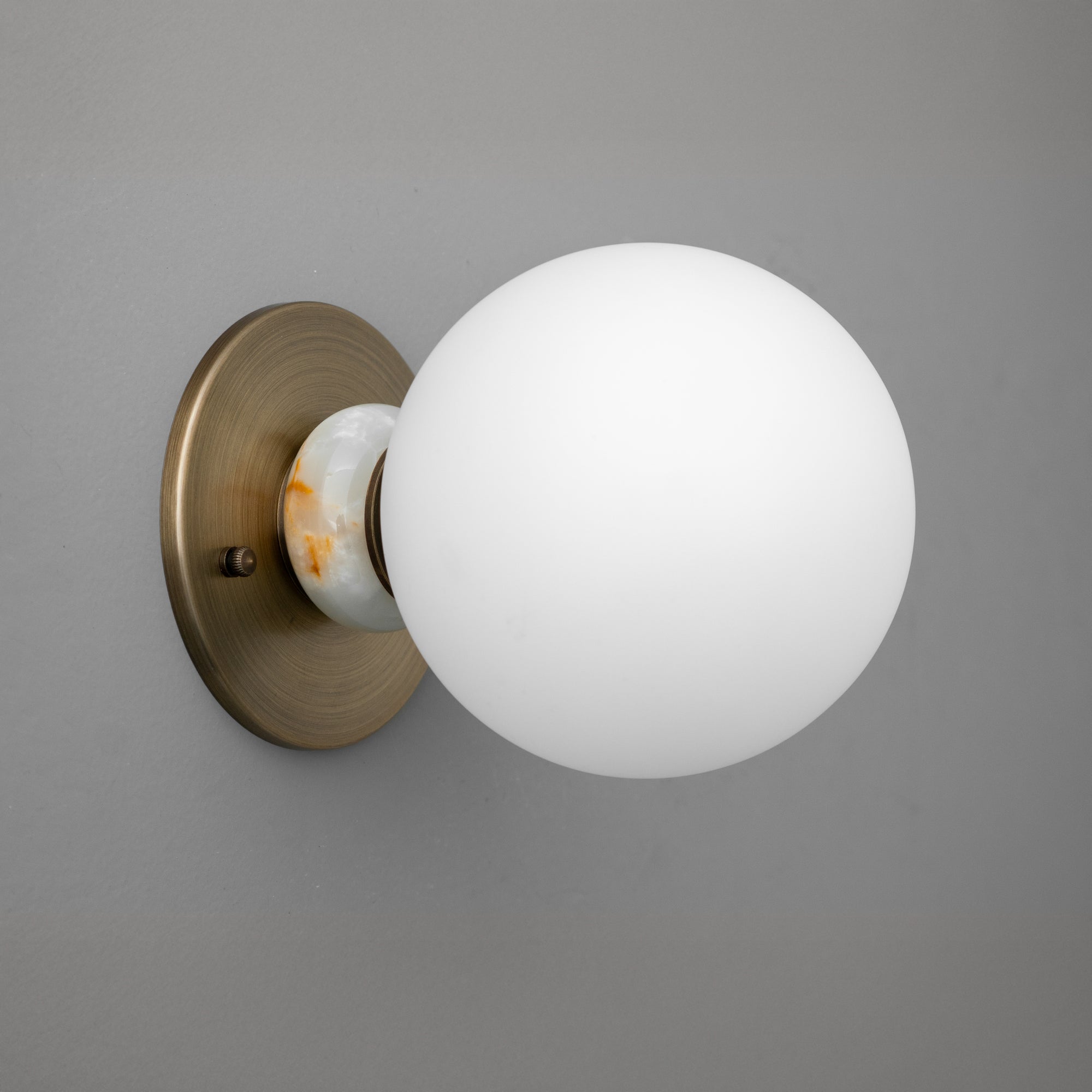 Minimalist antique brass wall sconce with frosted white glass globe shade on gray background. - SCONCE MODEL NO. 1246