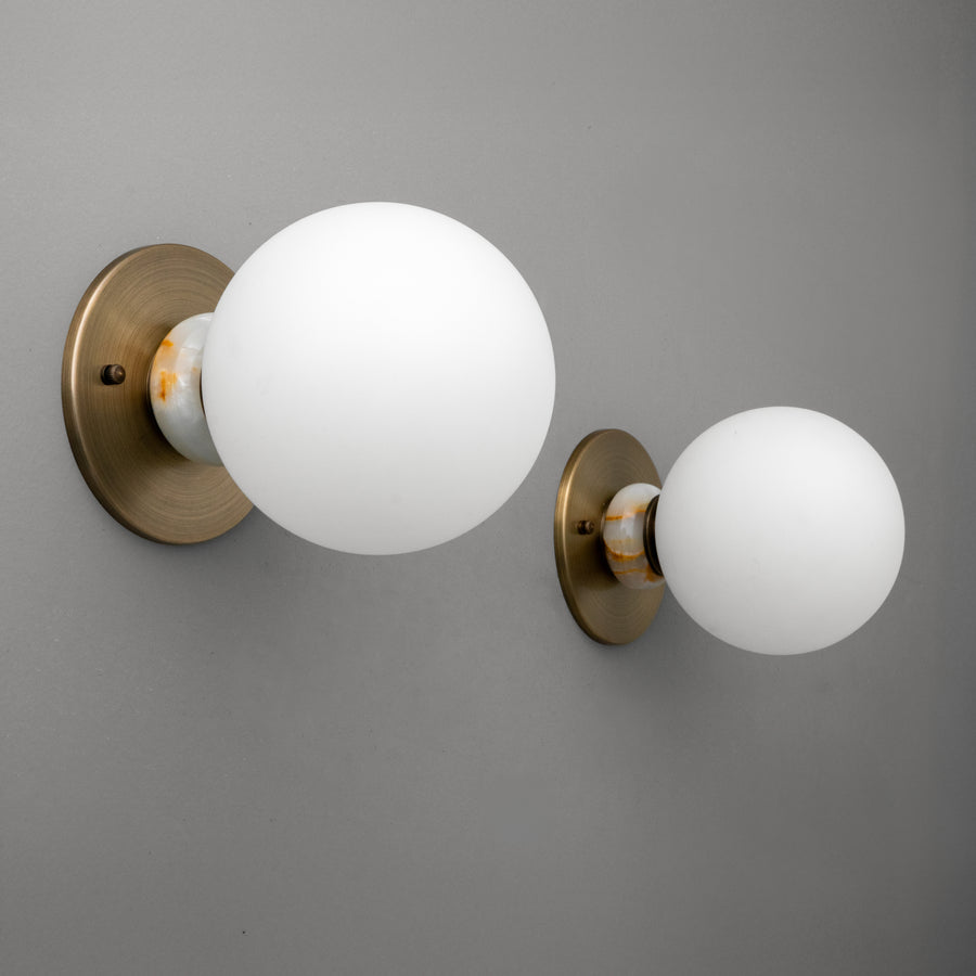 Two antique brass wall sconces with frosted white globe shades mounted on a gray wall. - SCONCE MODEL NO. 1246