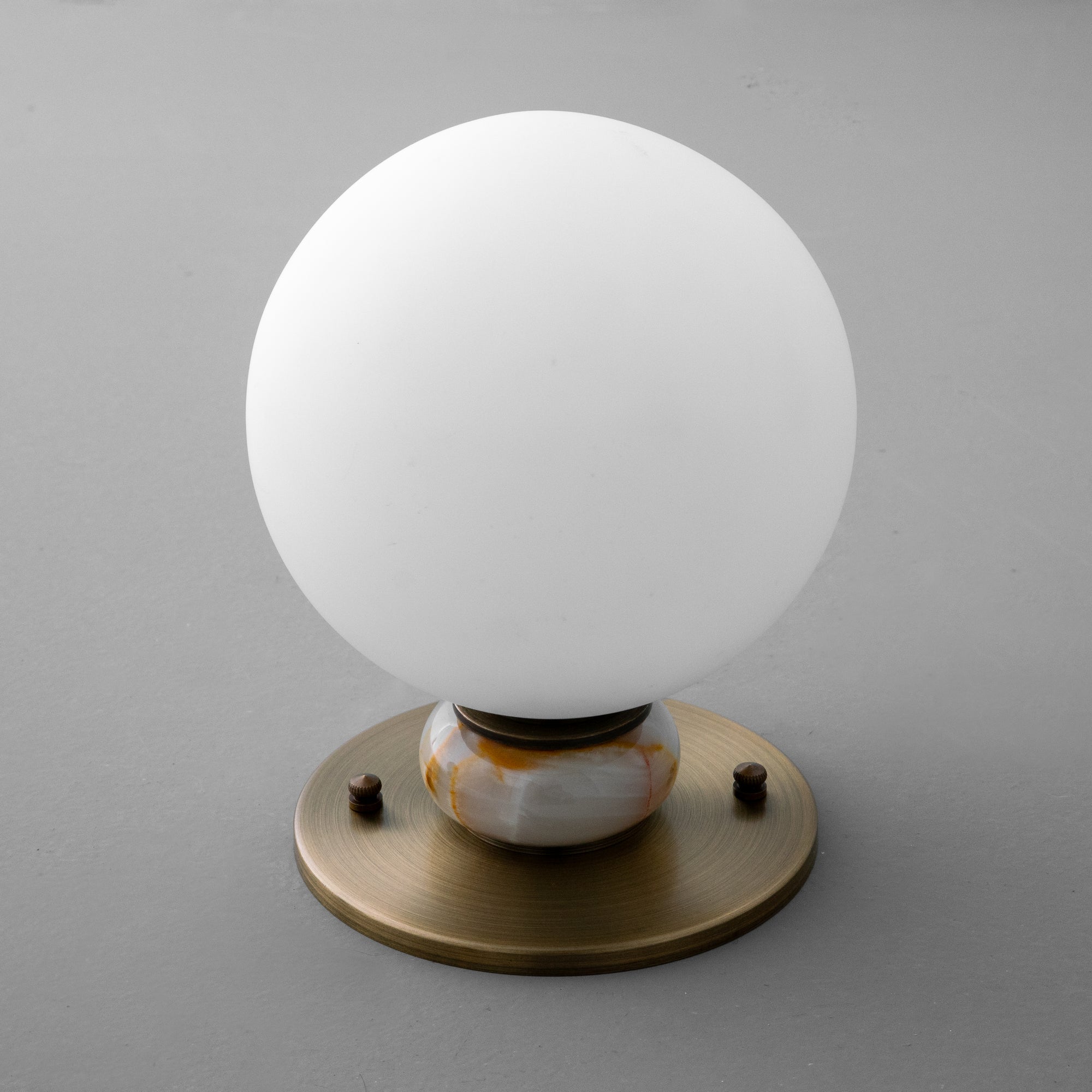 Minimalist wall sconce with a matte white globe and antique brass base on gray wall. - SCONCE MODEL NO. 1246