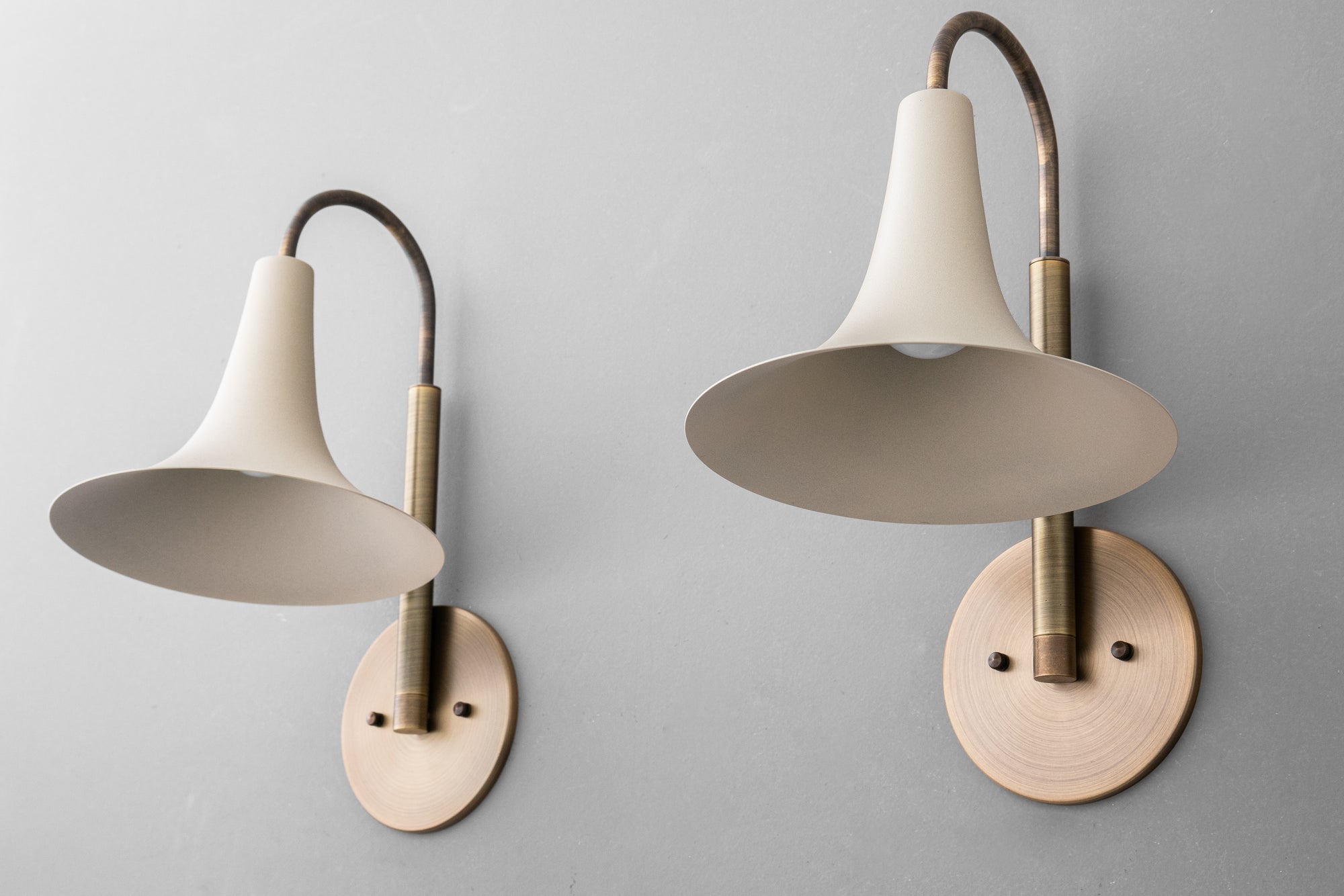 Pair of antique brass wall sconces with cream bell-shaped shades and round backplates on gray wall. - SCONCE MODEL NO. 3851