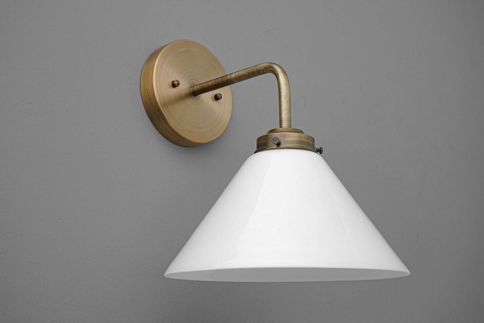 Wall-mounted antique brass sconce with white conical shade and curved arm on gray background. - SCONCE MODEL NO. 8751