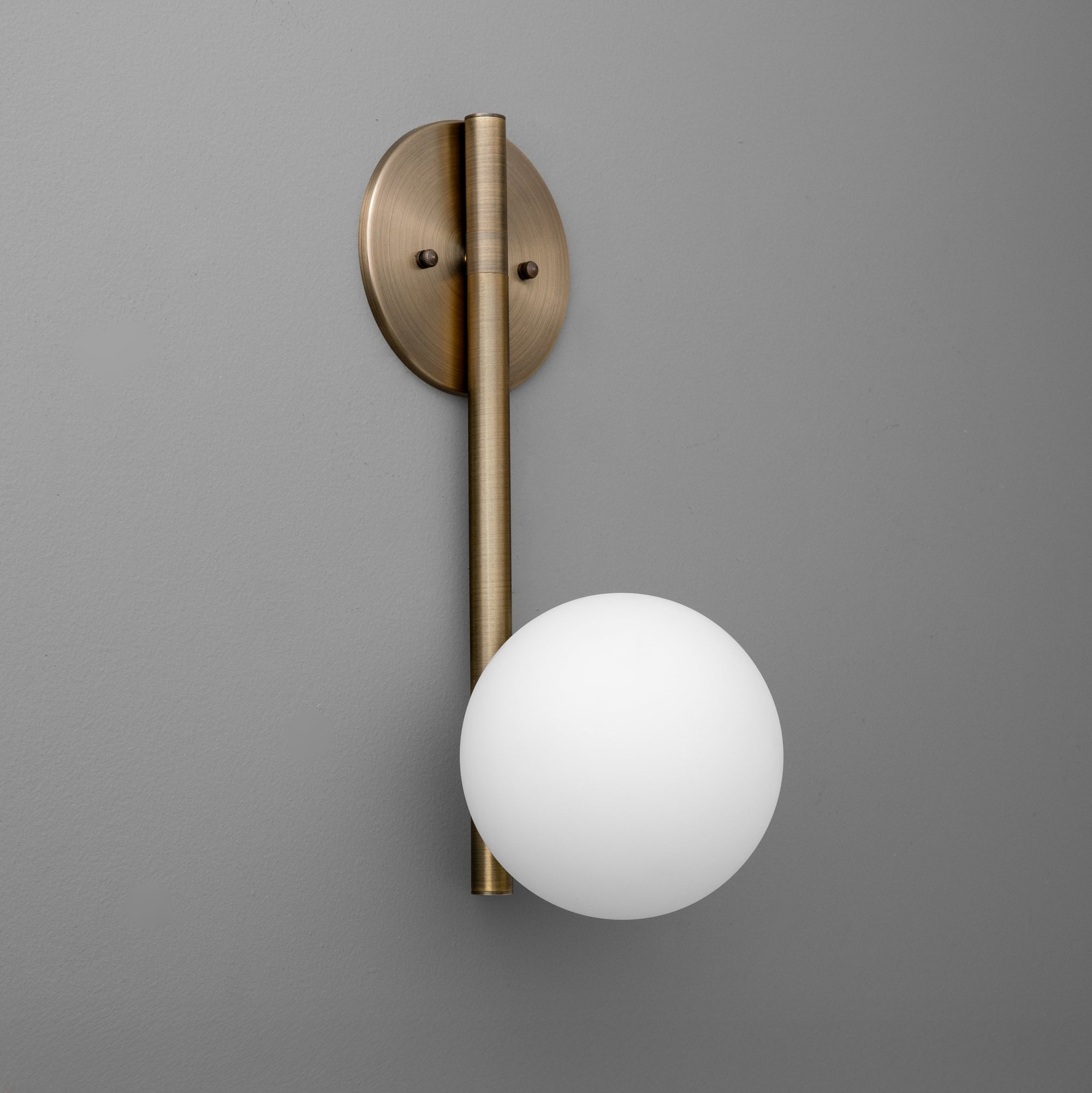 Antique brass wall sconce with vertical rod and round white glass globe shade on gray background. - SCONCE MODEL NO. 0981