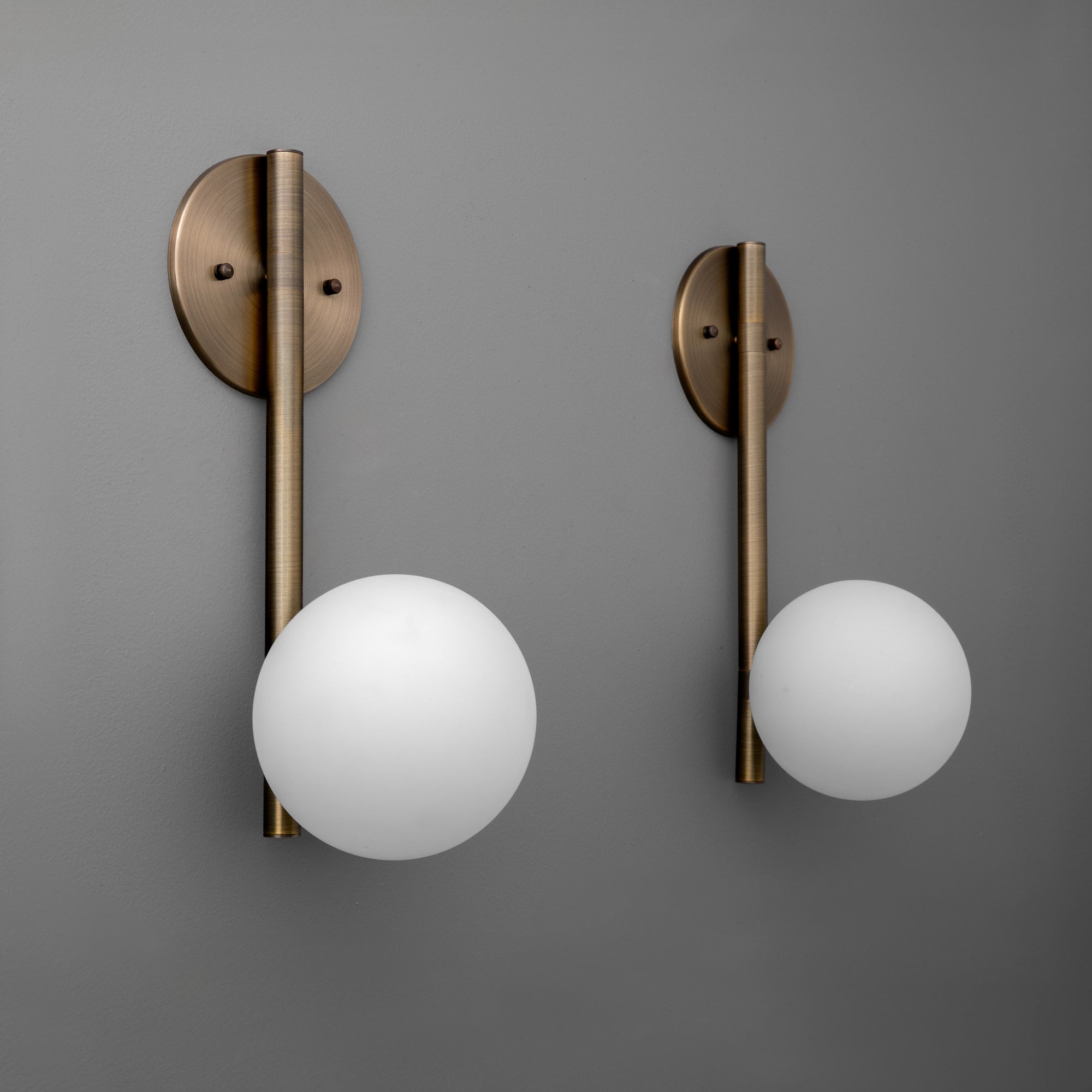 Antique brass wall sconces with round white glass globes and minimalist vertical rods on gray background. - SCONCE MODEL NO. 0981