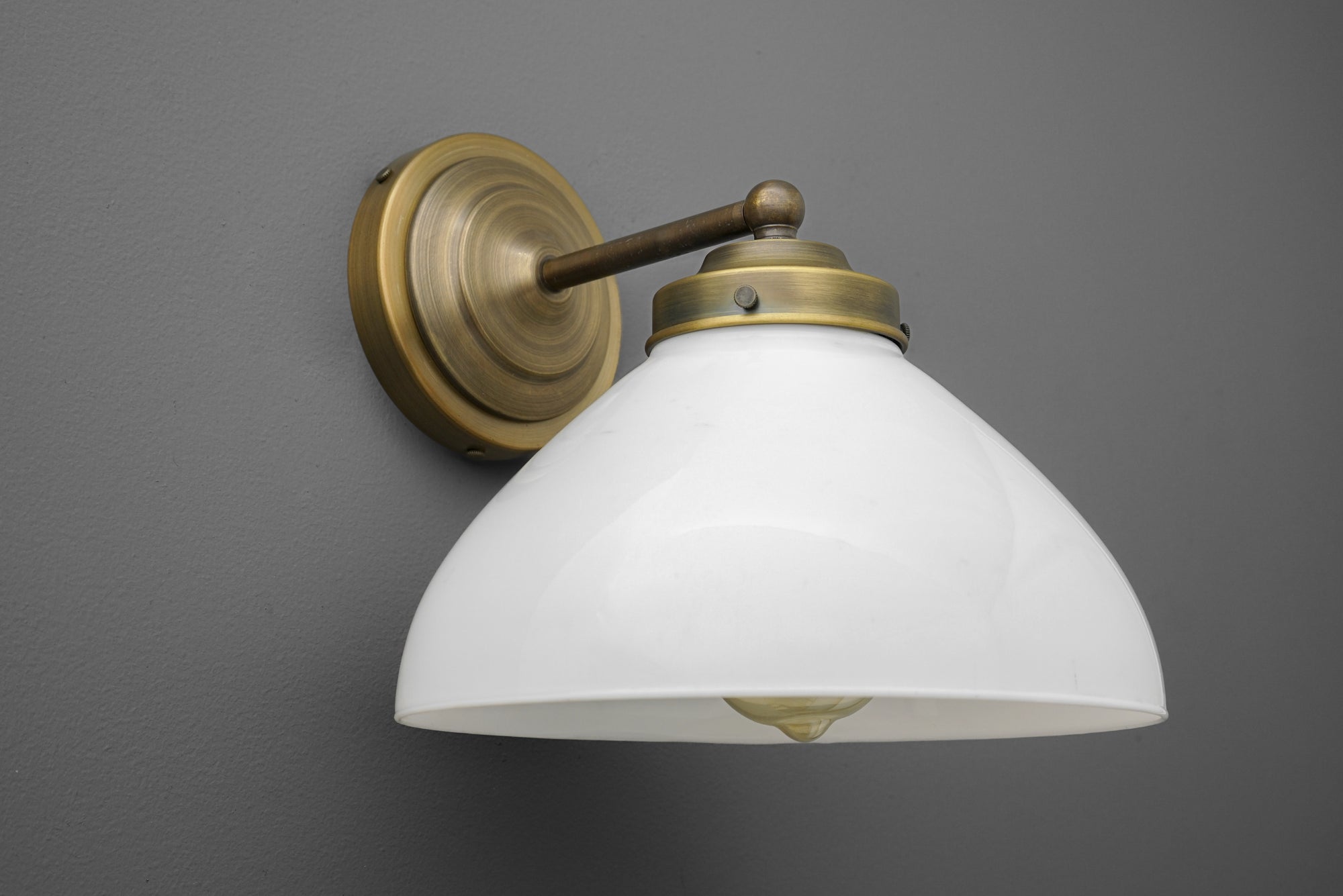 Wall sconce with antique brass finish and white glass dome shade mounted on gray wall. - SCONCE MODEL NO. 9835