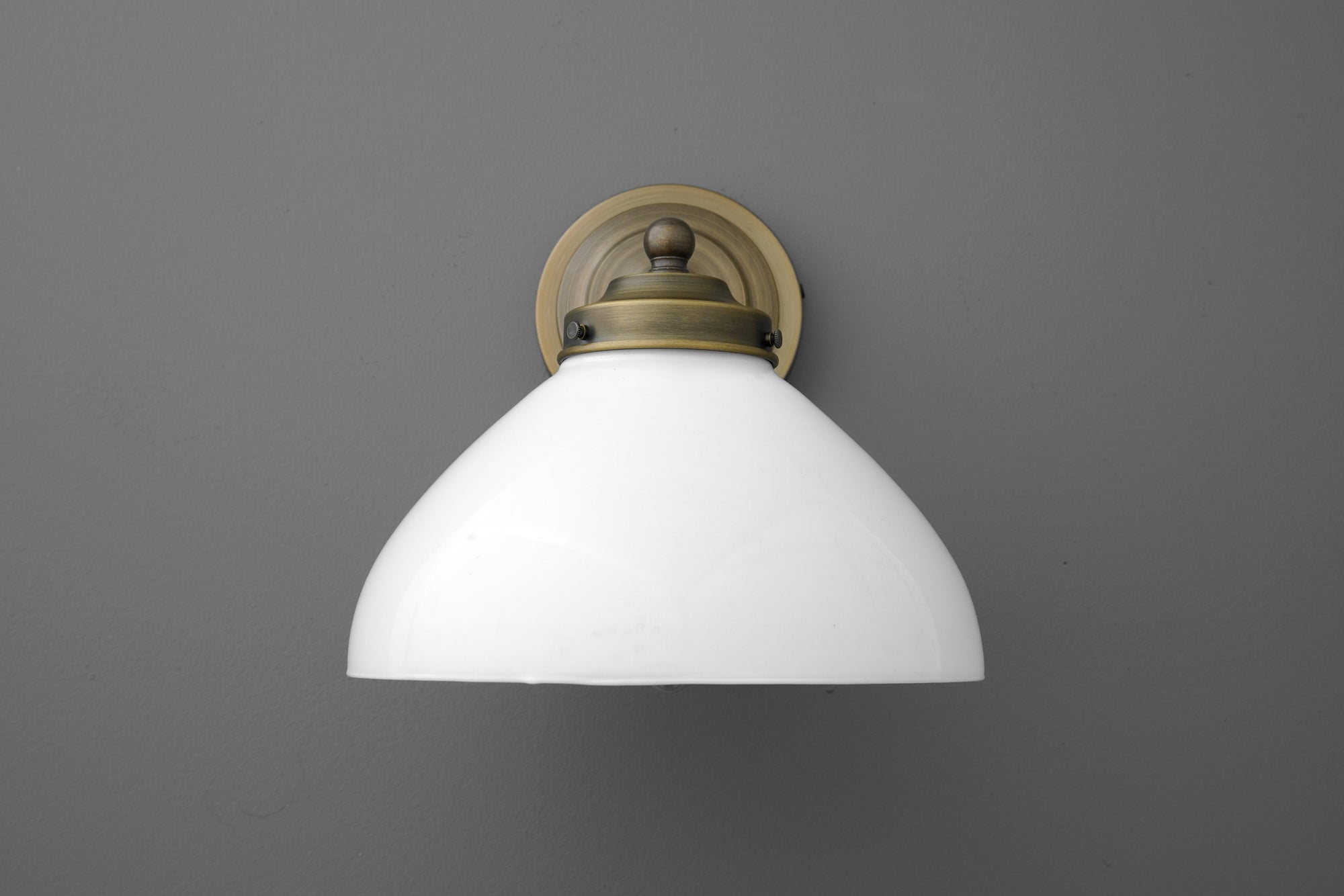 Wall sconce with antique brass finish and white curved glass shade against gray background. - SCONCE MODEL NO. 9835