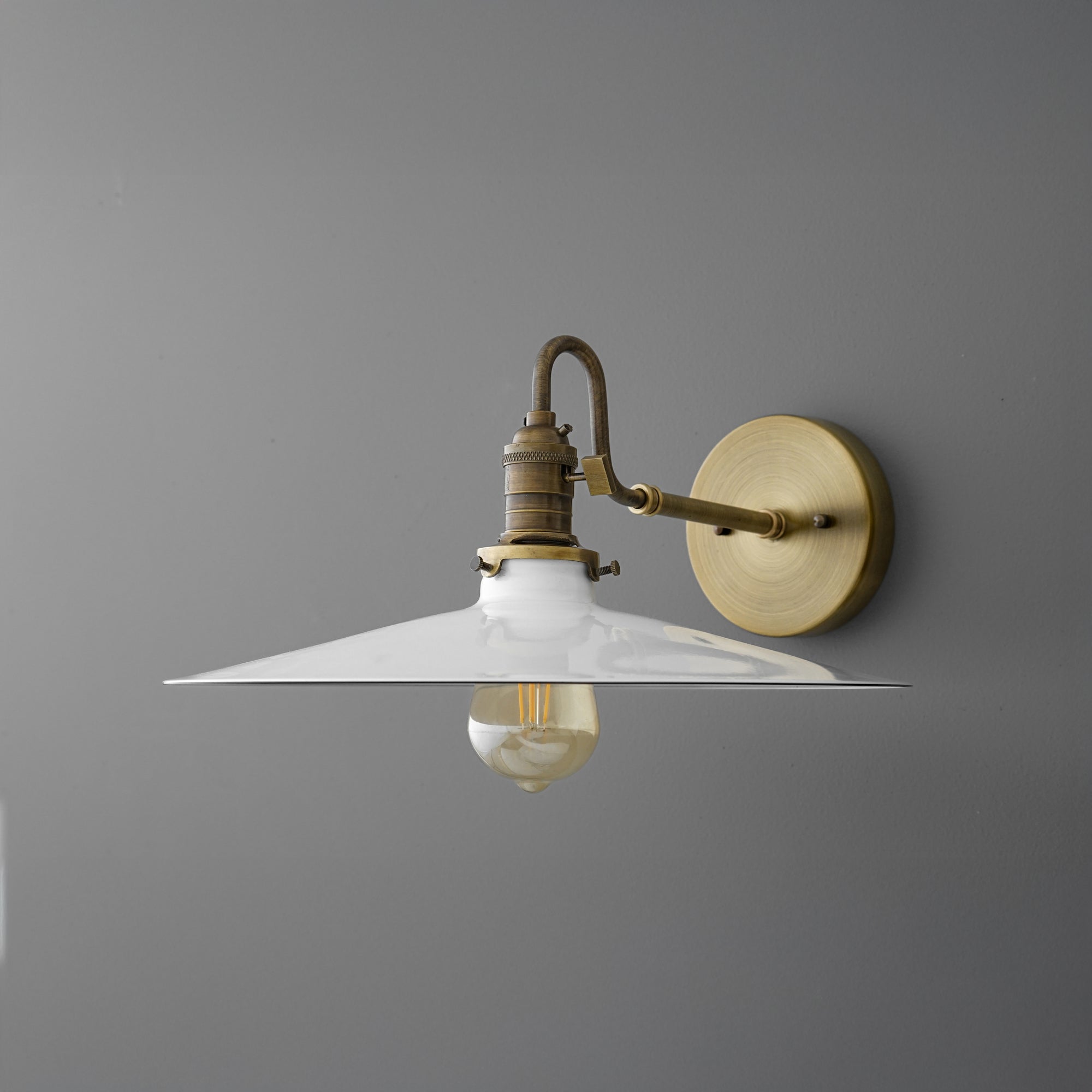 Brass wall sconce with wide white metal shade and exposed Edison bulb on gray wall. - SCONCE MODEL NO. 5562