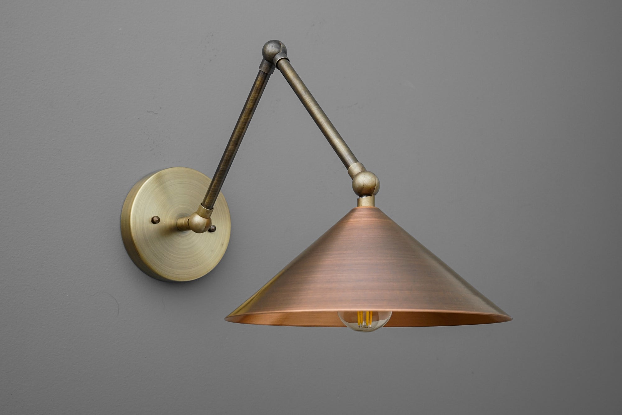 Adjustable wall sconce with conical copper shade and articulated brass arm against gray background. - SCONCE MODEL NO. 6414