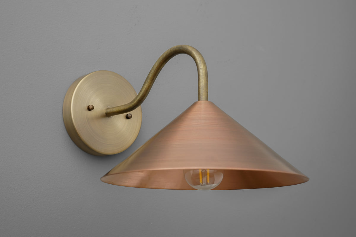 Wall sconce with antique brass arm and wide conical copper shade on gray background. - SCONCE MODEL NO. 7574