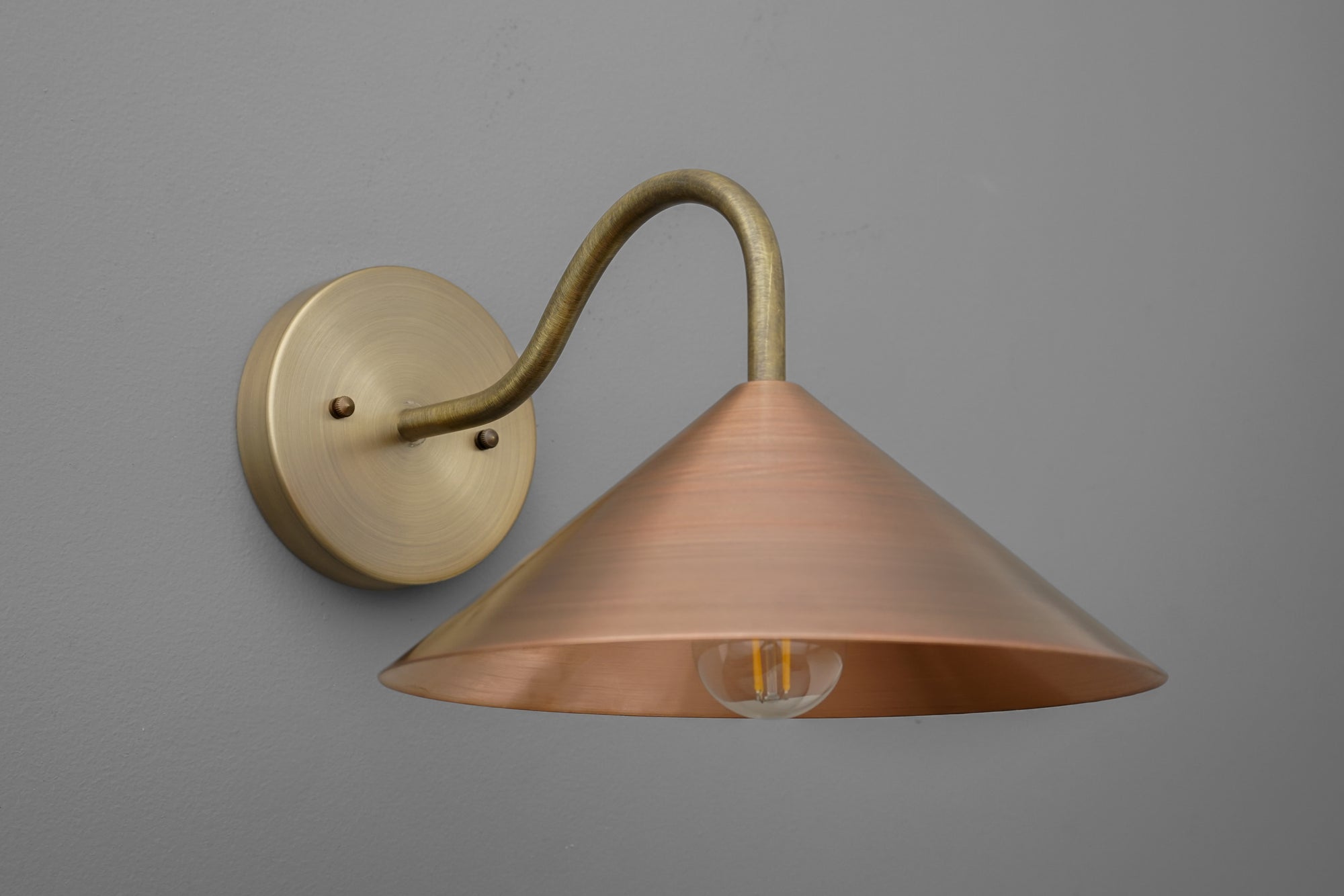 Wall sconce with antique brass arm and wide conical copper shade on gray background. - SCONCE MODEL NO. 7574