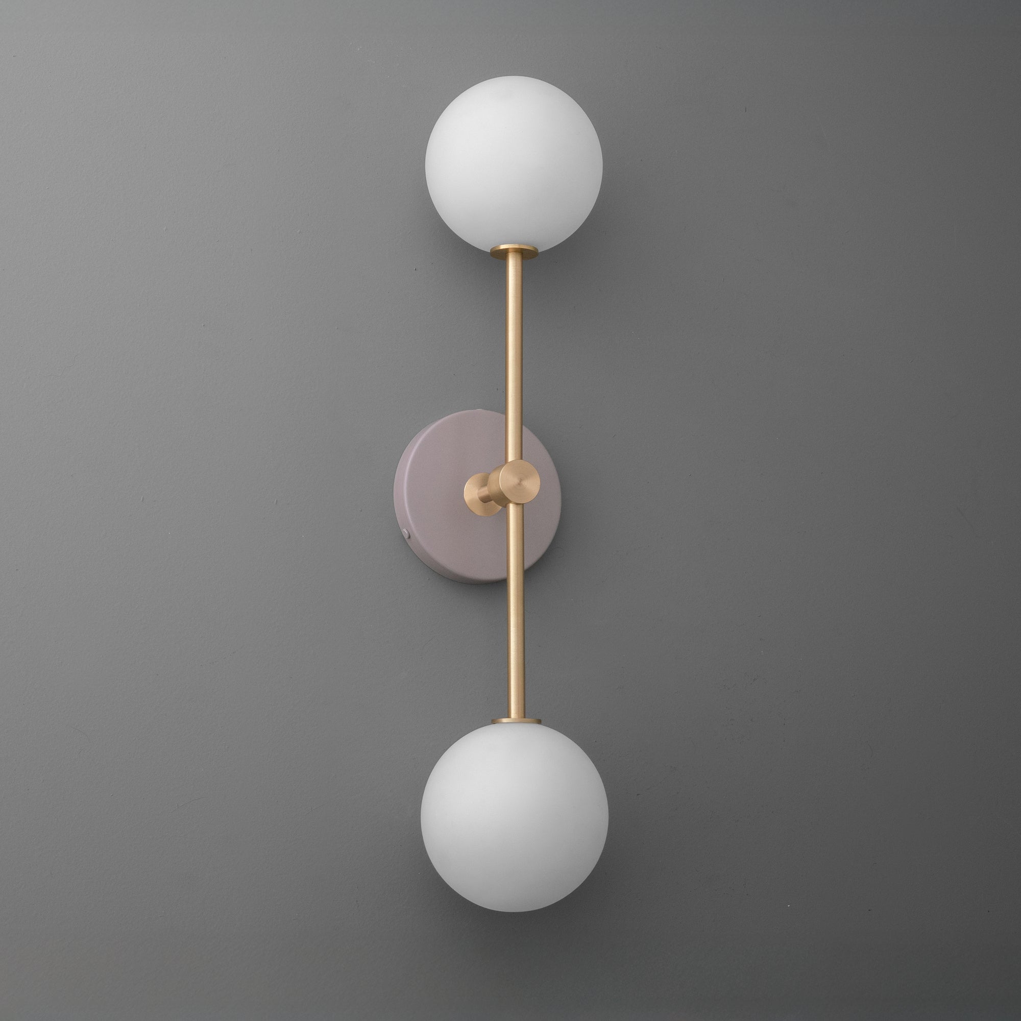 Wall sconce with raw brass finish, mauve circular backplate, and two white frosted glass globes. - SCONCE MODEL NO. 9776