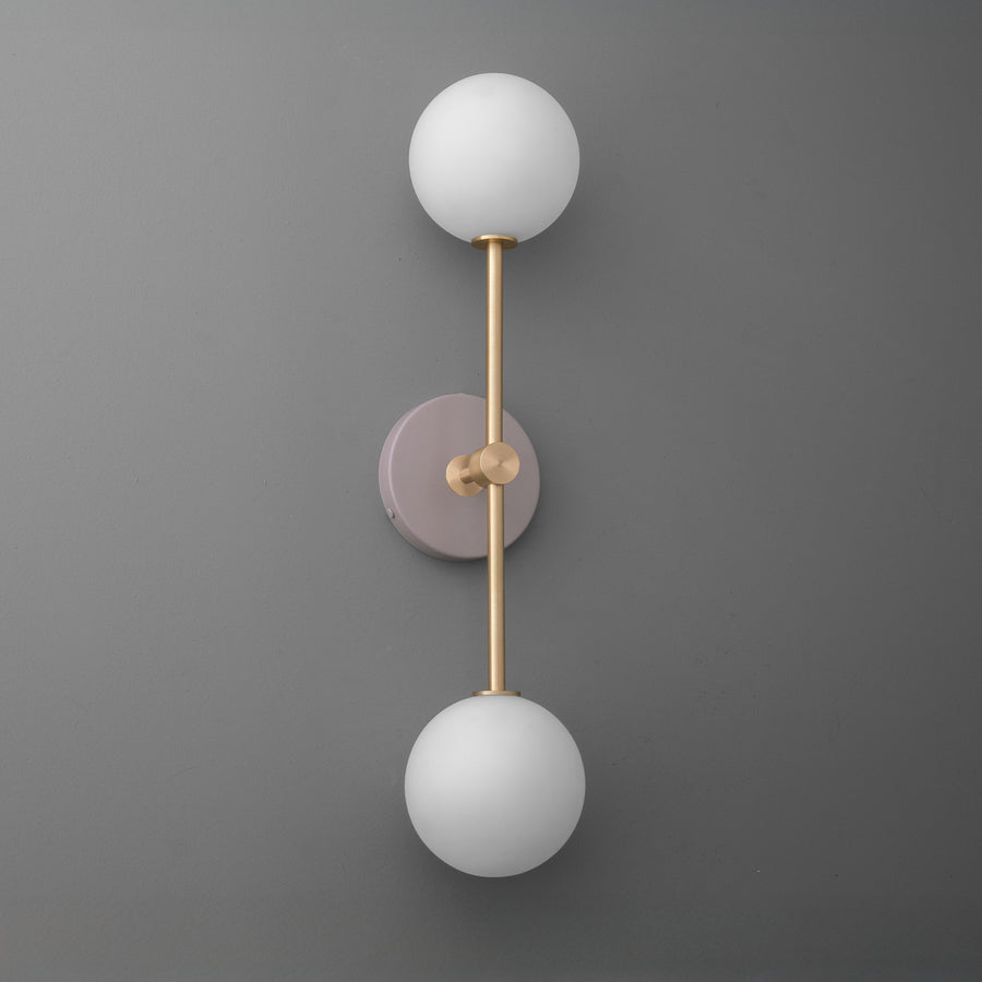 Wall sconce with raw brass finish, mauve circular backplate, and two white frosted glass globes. - SCONCE MODEL NO. 9776