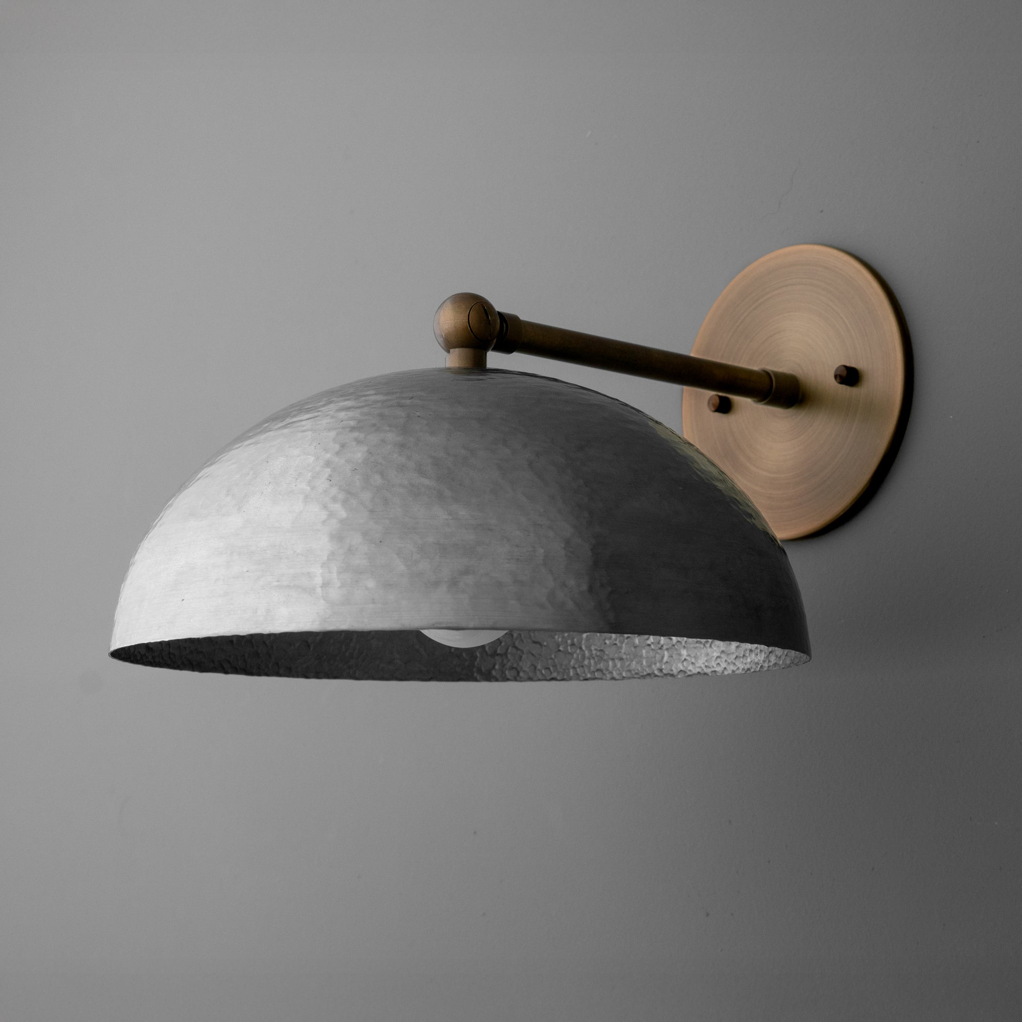 Wall sconce with aged steel dome shade and antique brass round wall plate on gray background. - SCONCE MODEL NO. 3164