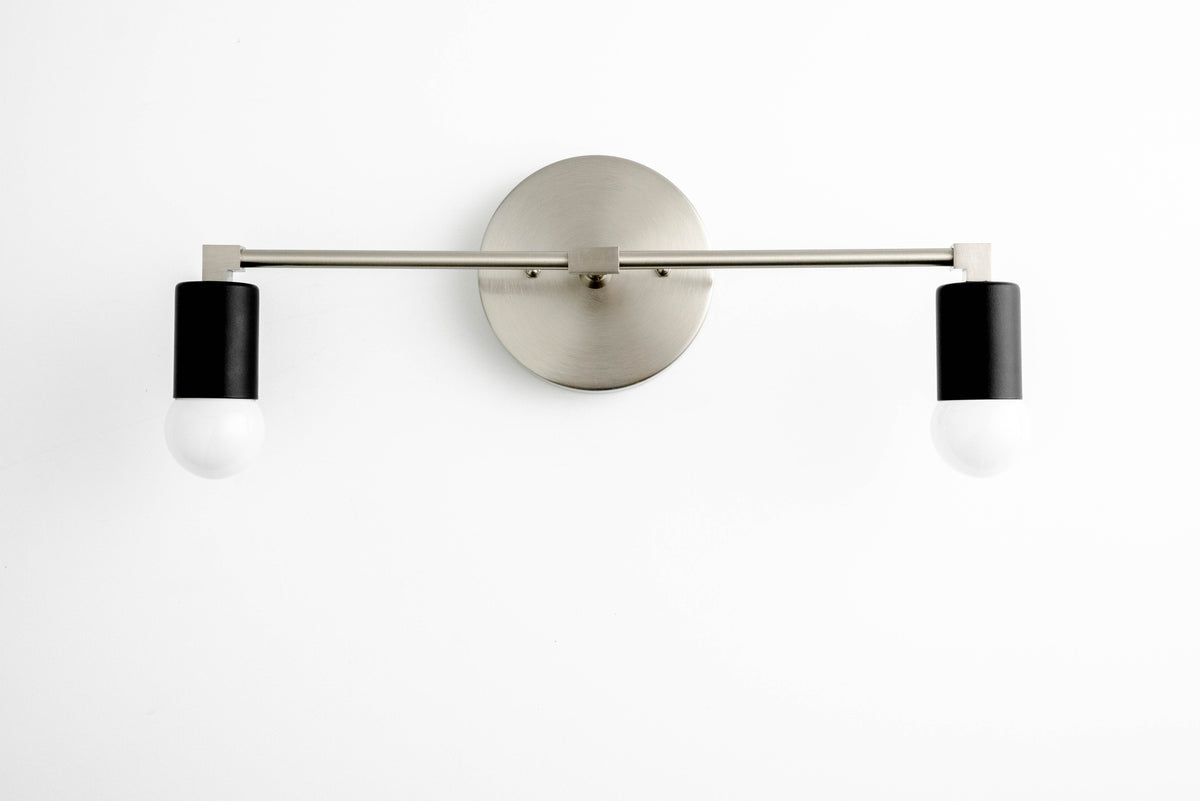 Two-light vanity light in Brushed Nickel/Black, with a Brushed Nickel wall plate and bar and Black sockets. - VANITY LIGHT MODEL NO. 8412