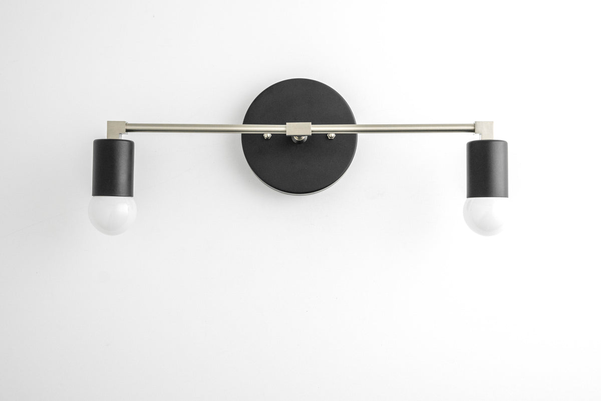 Two-light vanity light in Black/Br. Nickel/Black, with a Black wall plate and sockets on a Brushed Nickel bar. - VANITY LIGHT MODEL NO. 8412