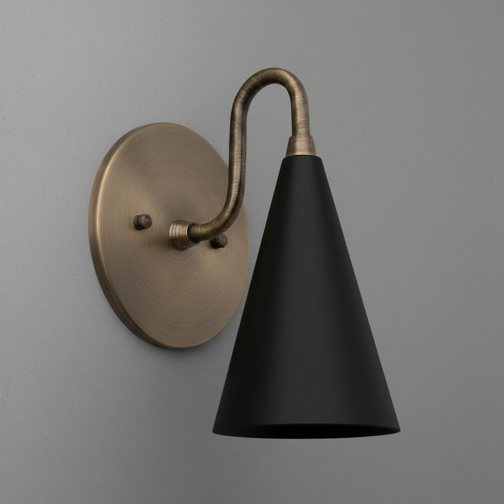 Antique brass wall sconce with matte black conical shade and curved arm on gray wall. - Sconce Model No. 2900