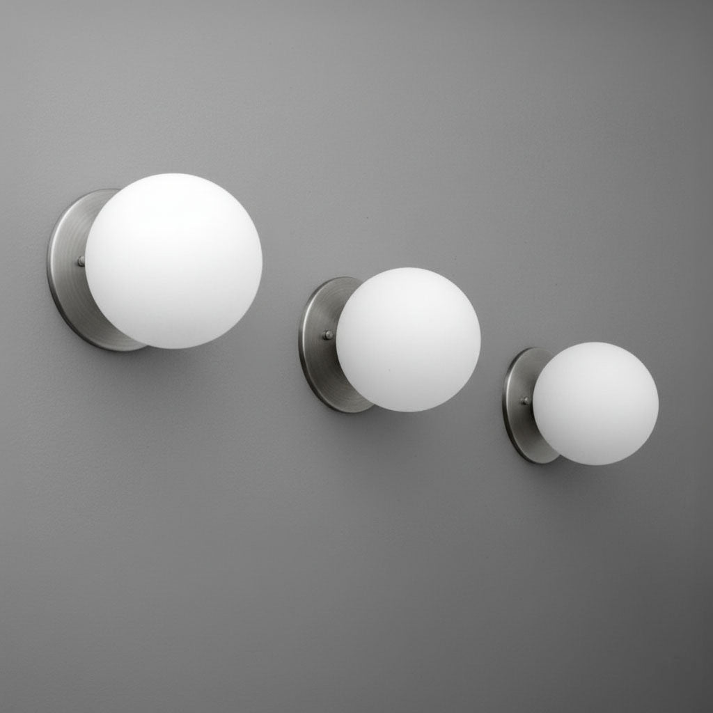 Three brushed nickel wall sconces with frosted white glass globes mounted on a gray wall in varying sizes. - Sconce Model No. 5206