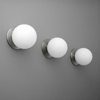 Three brushed nickel wall sconces with frosted white glass globes mounted on a gray wall in varying sizes. - Sconce Model No. 5206