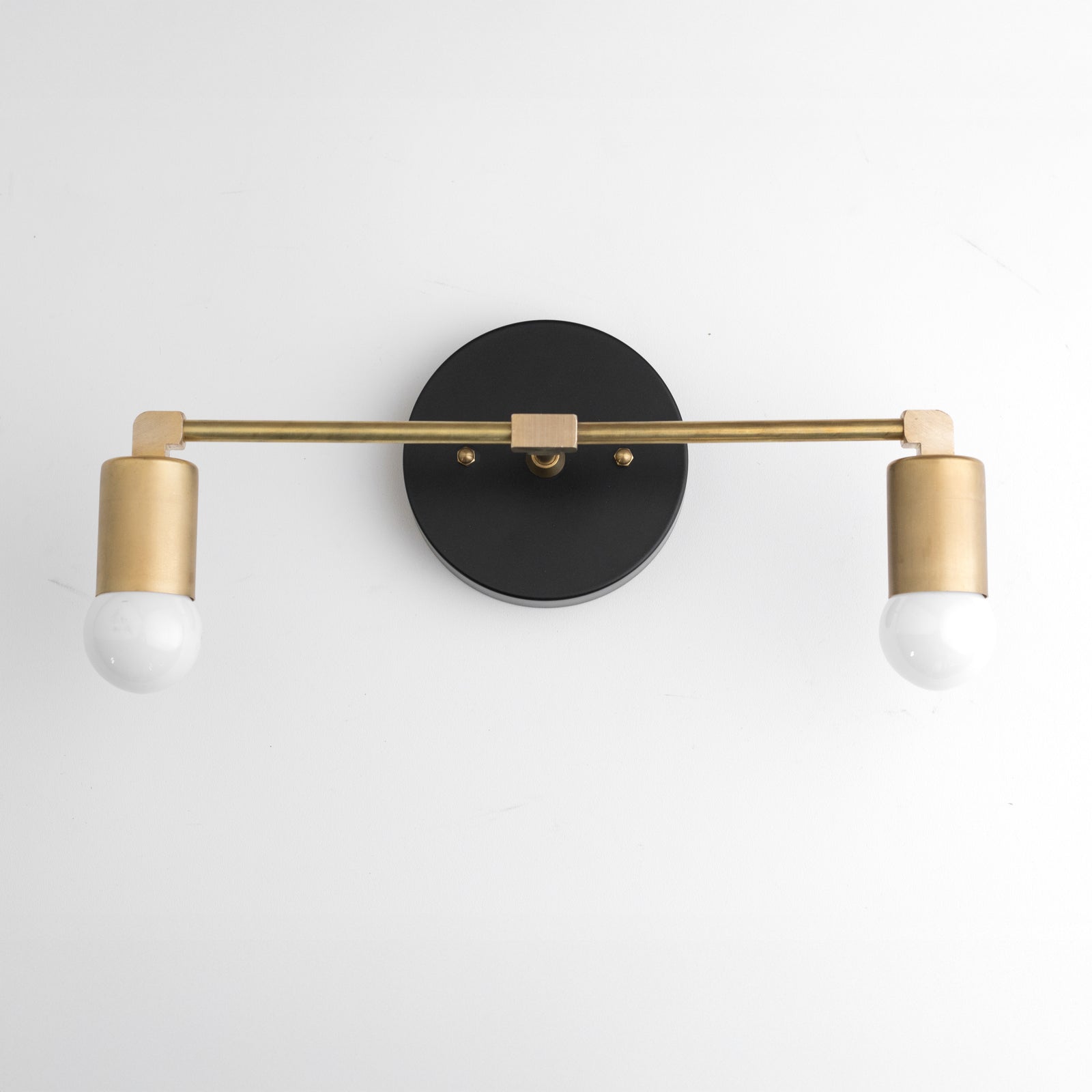 Two-light vanity light with a Black round wall plate and a Raw or Sealed Brass bar and sockets, bare globe bulbs. - VANITY LIGHT MODEL NO. 8412
