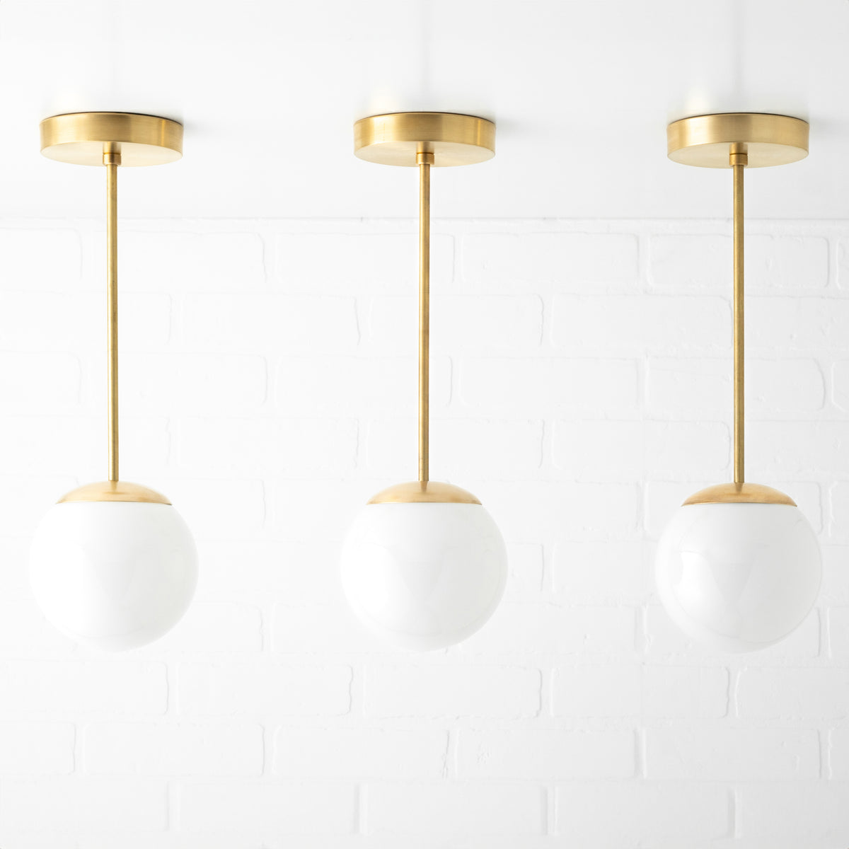 Set of three mid-century modern pendant lights with white glass globe shades and brushed brass fixtures. - PENDANT MODEL NO. 7056