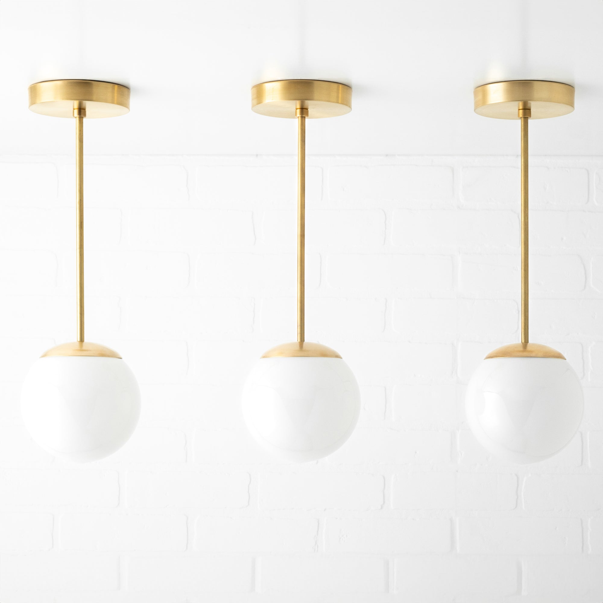 Set of three mid-century modern pendant lights with white glass globe shades and brushed brass fixtures. - PENDANT MODEL NO. 7056