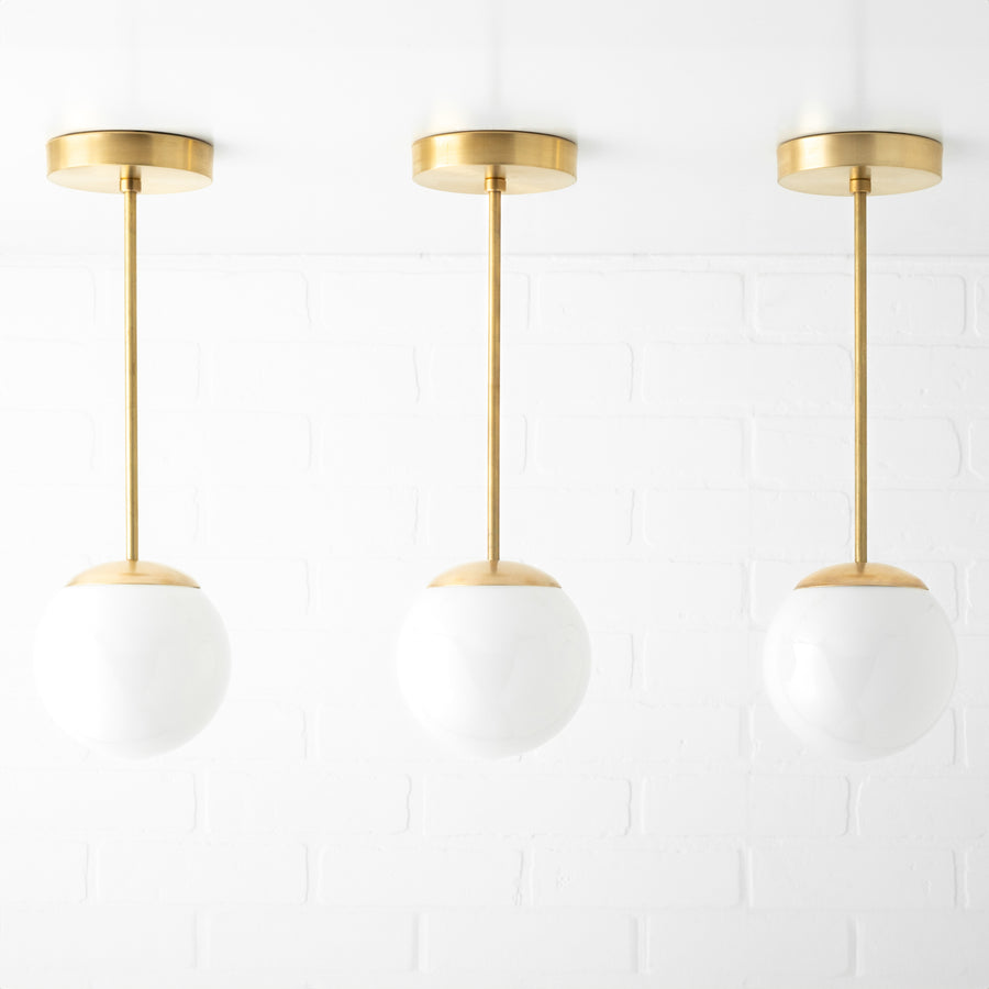 Set of three mid-century modern pendant lights with white glass globe shades and brushed brass fixtures. - PENDANT MODEL NO. 7056
