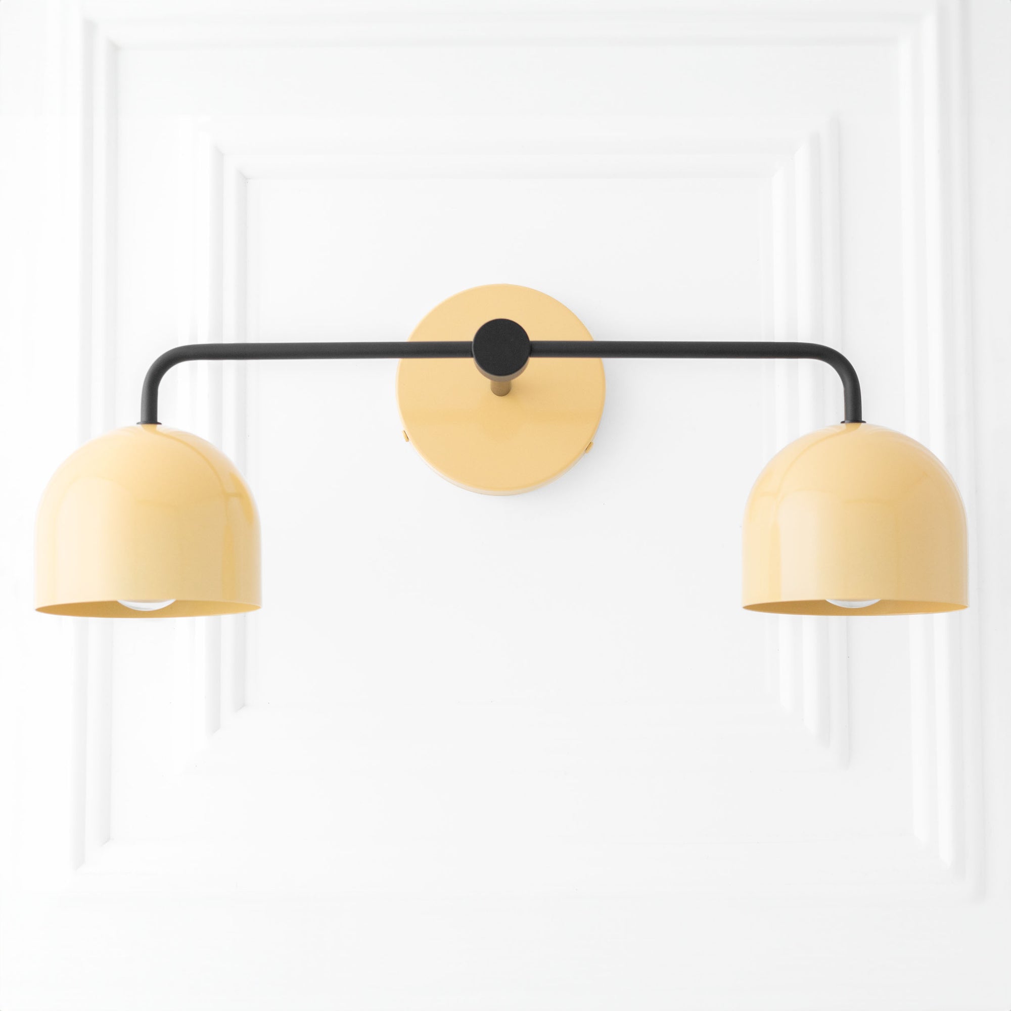 Mid-century modern vanity light with two rounded beige metal shades and black horizontal arm mounted on round beige wall. - VANITY LIGHT MODEL NO. 2082