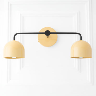 Mid-century modern vanity light with two rounded beige metal shades and black horizontal arm mounted on round beige wall. - VANITY LIGHT MODEL NO. 2082