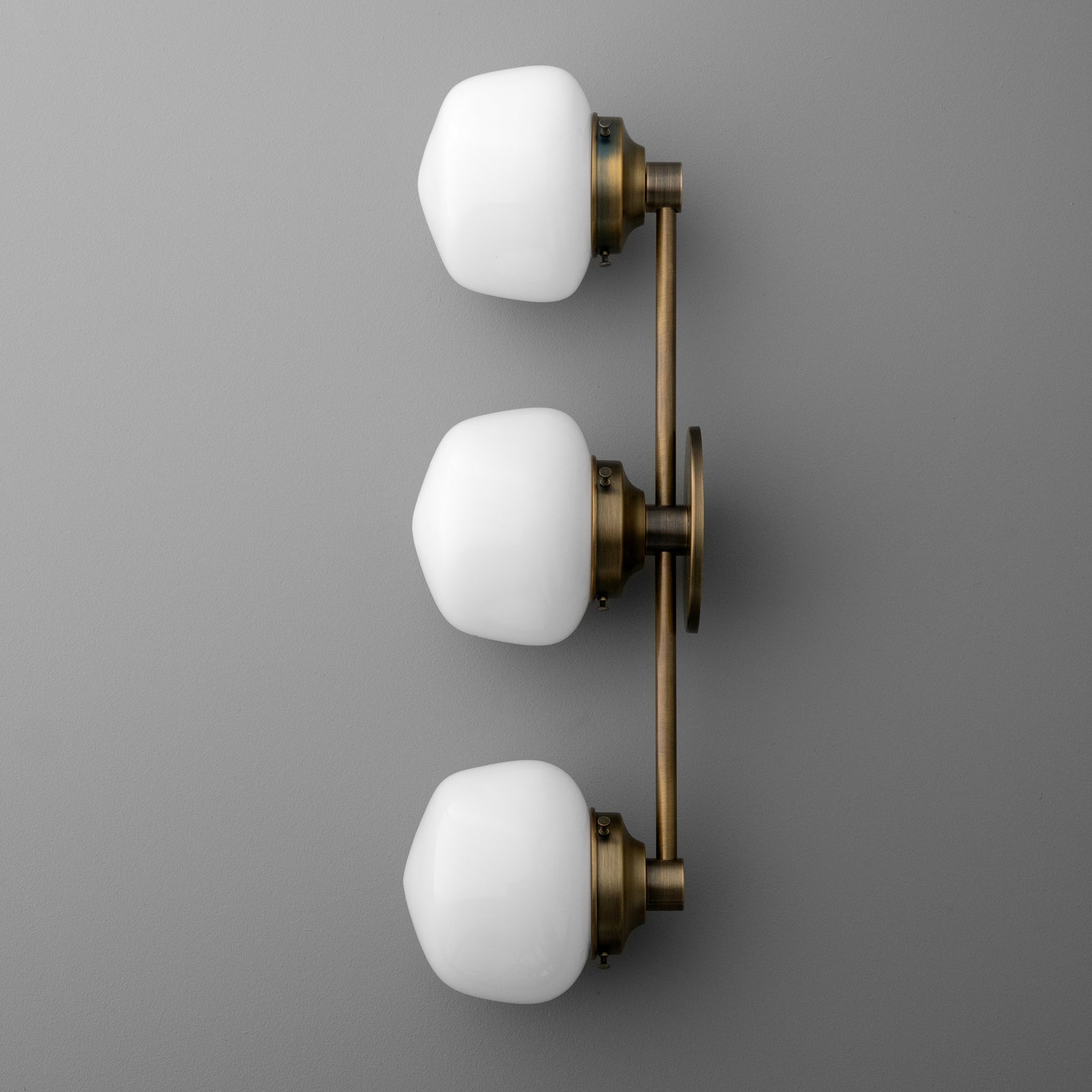 Three-bulb vanity light with white frosted glass shades and antique brass mounting bar. - VANITY LIGHT MODEL NO. 1106