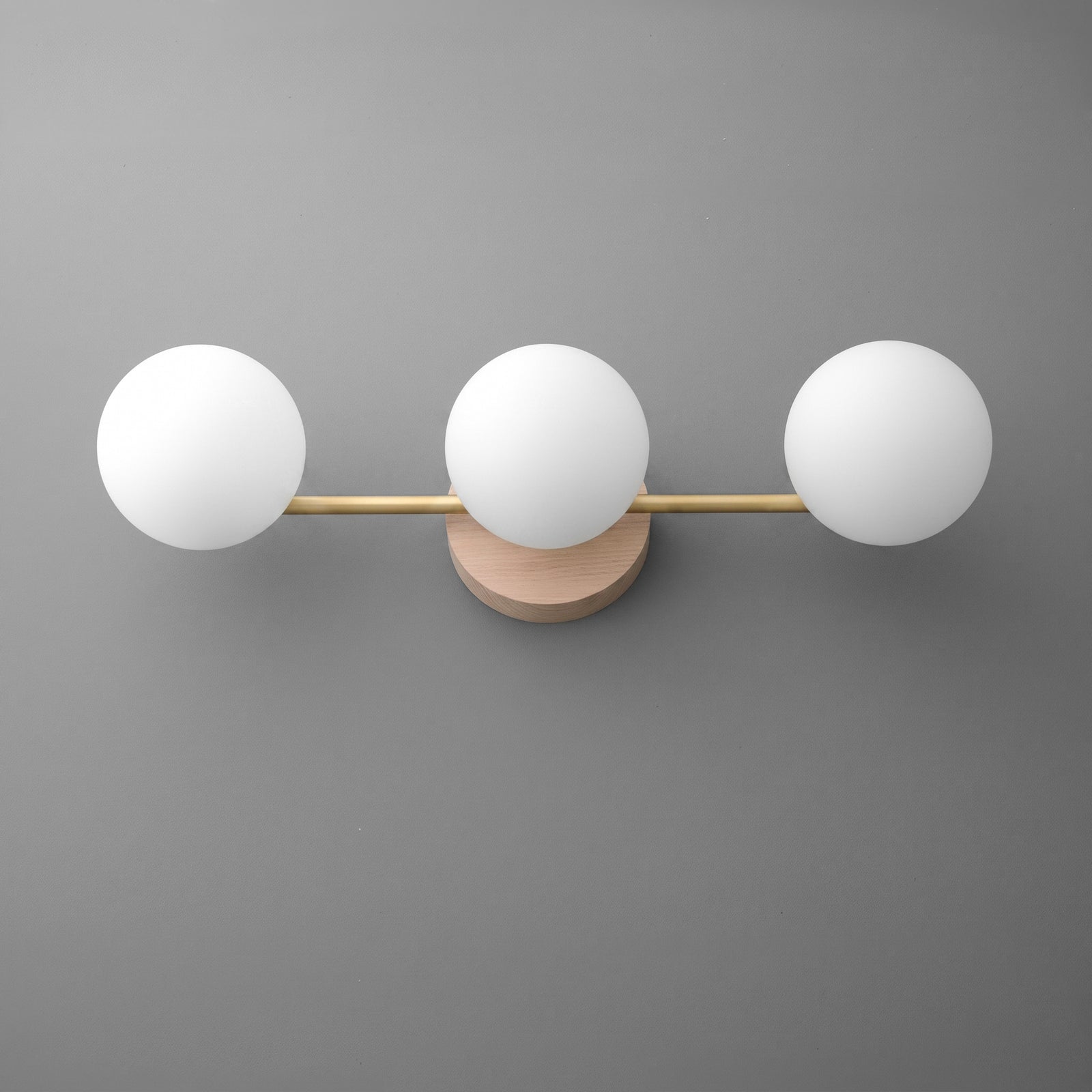 Wall-mounted vanity light with three frosted white glass globes and a brushed gold horizontal bar on a round beige base. - VANITY LIGHT MODEL NO. 6089