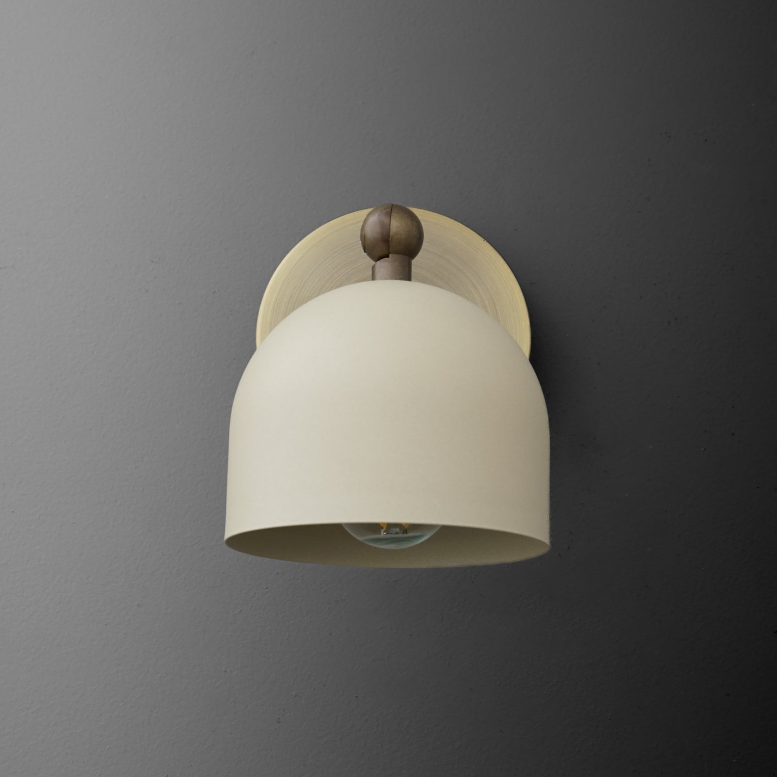 Antique brass wall sconce with cream-colored cylinder shade and round backplate on gray wall. - SCONCE MODEL NO. 5103