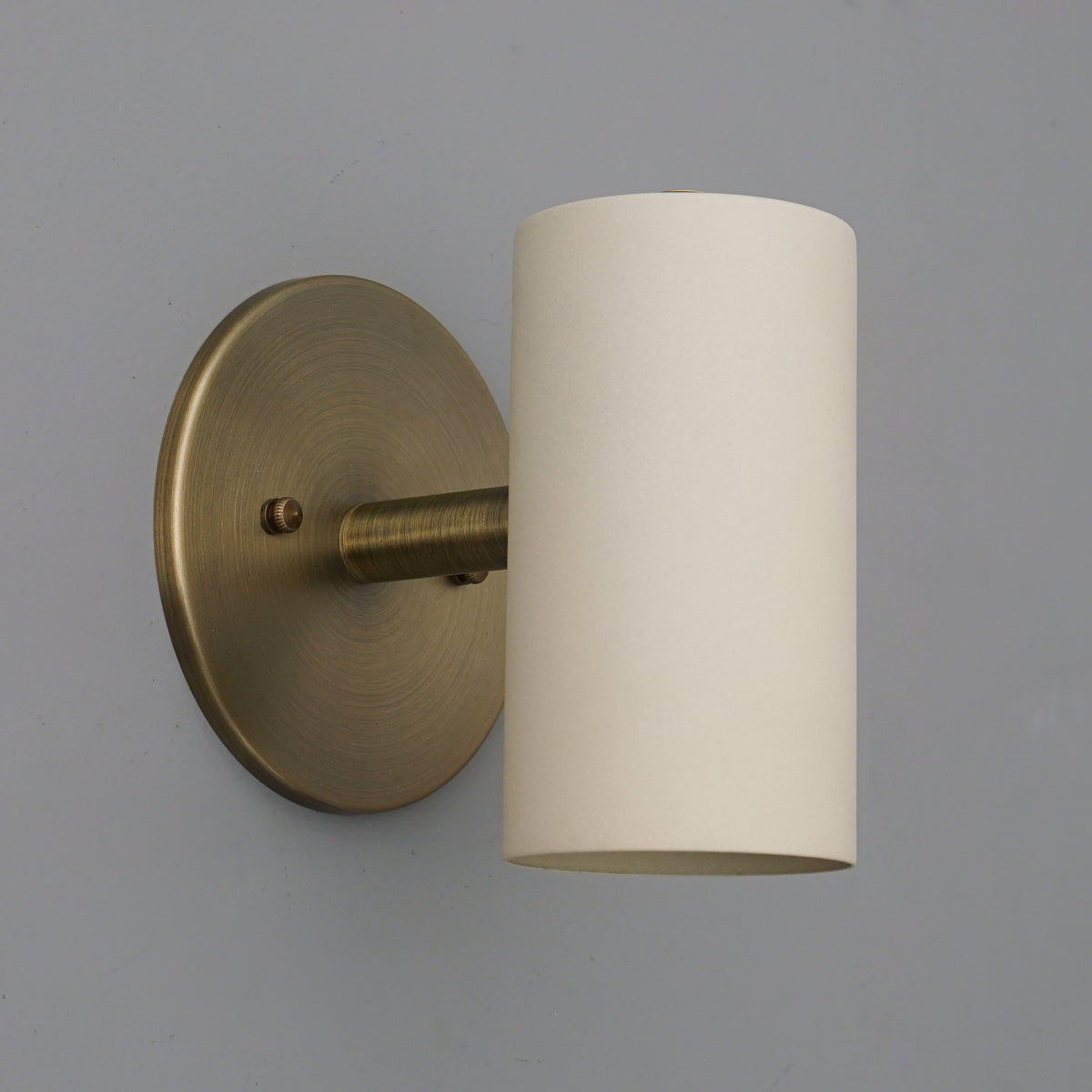 Cylinder sconce with a Cream shade on a short stem from an Antique Brass round wall plate. - SCONCE MODEL NO. 9697