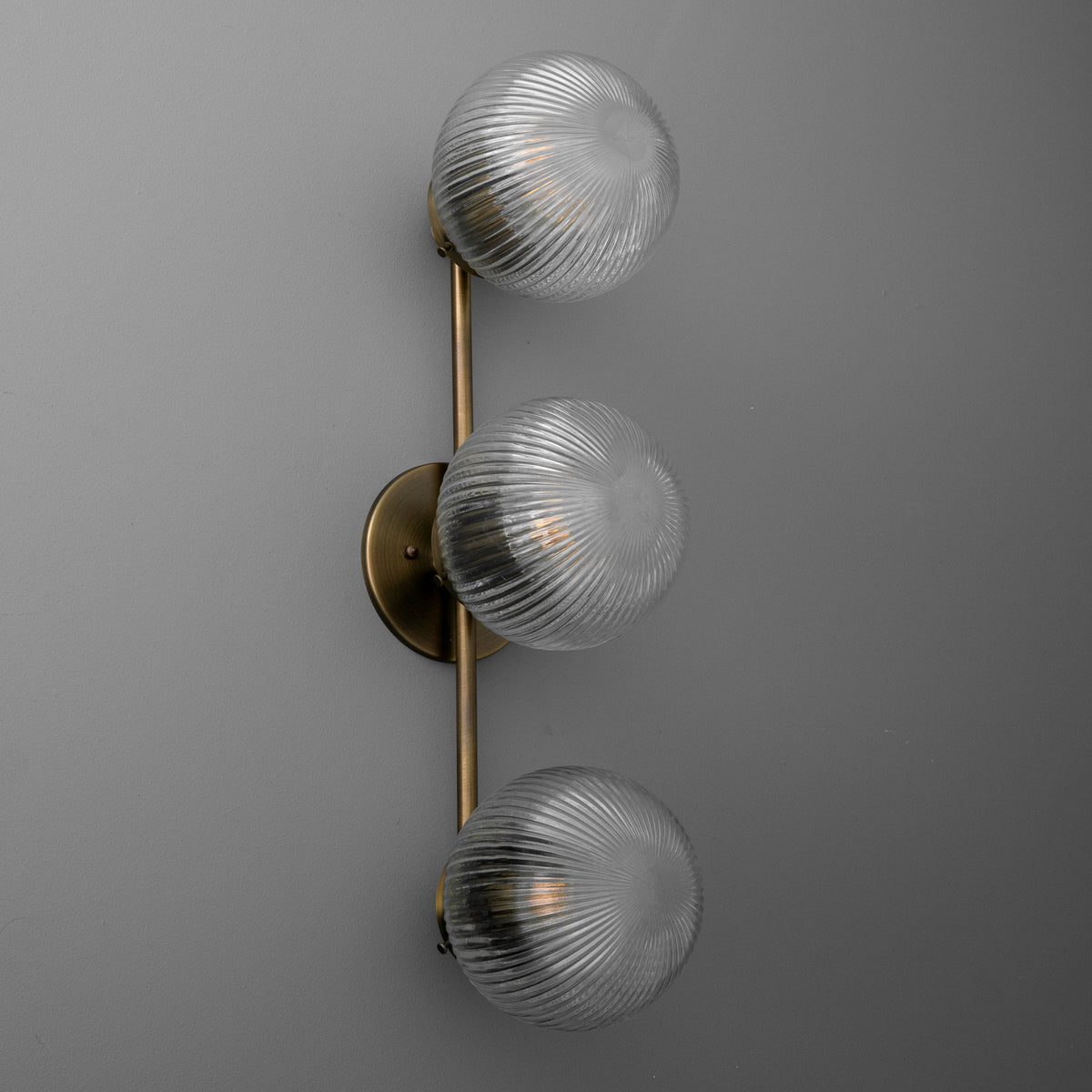 Three-bulb wall sconce with ribbed glass globes and antique brass vertical mounting plate. - SCONCE MODEL NO. 1108
