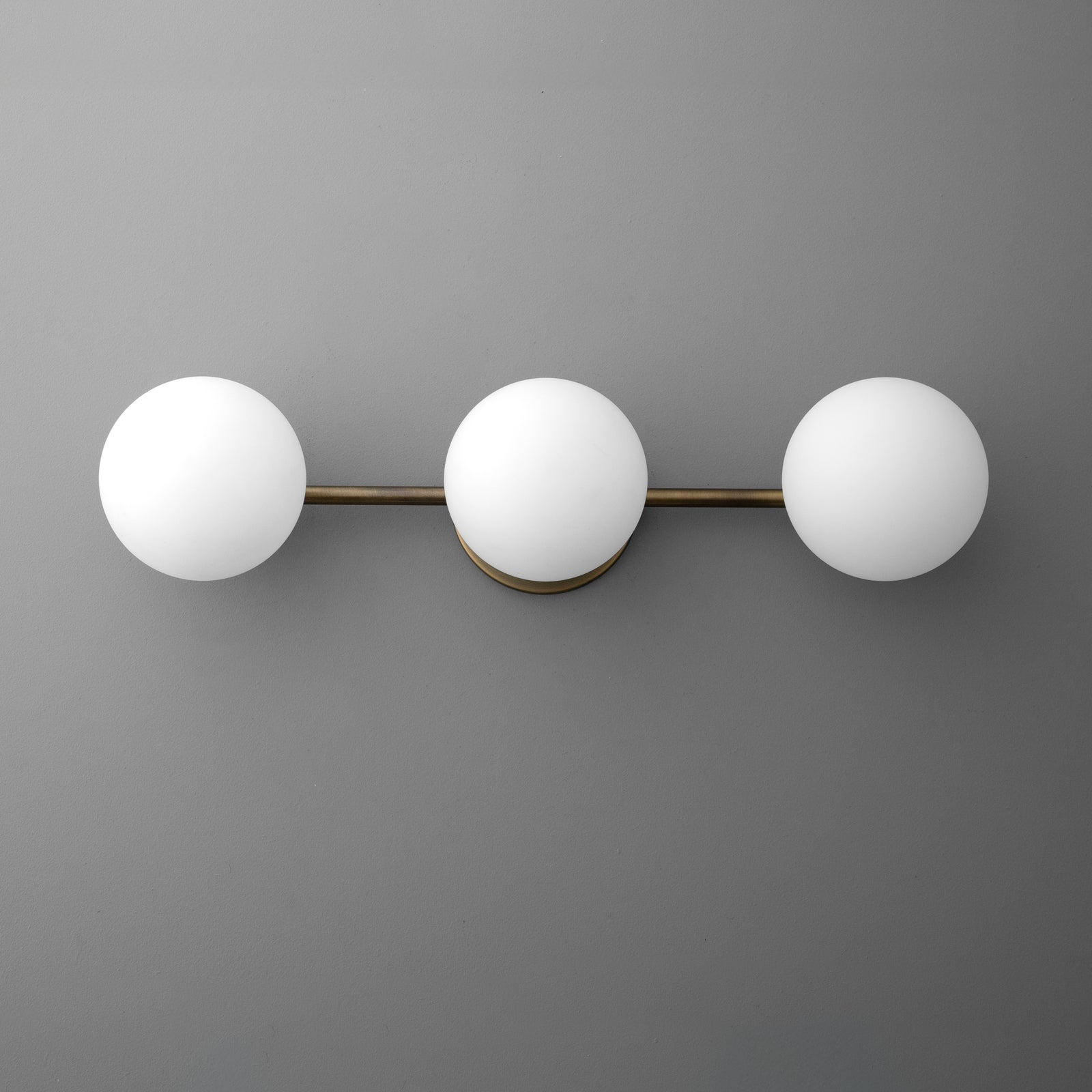 Three white globe lights on a horizontal brushed brass fixture mounted on a gray wall. - VANITY LIGHT MODEL NO. 9250