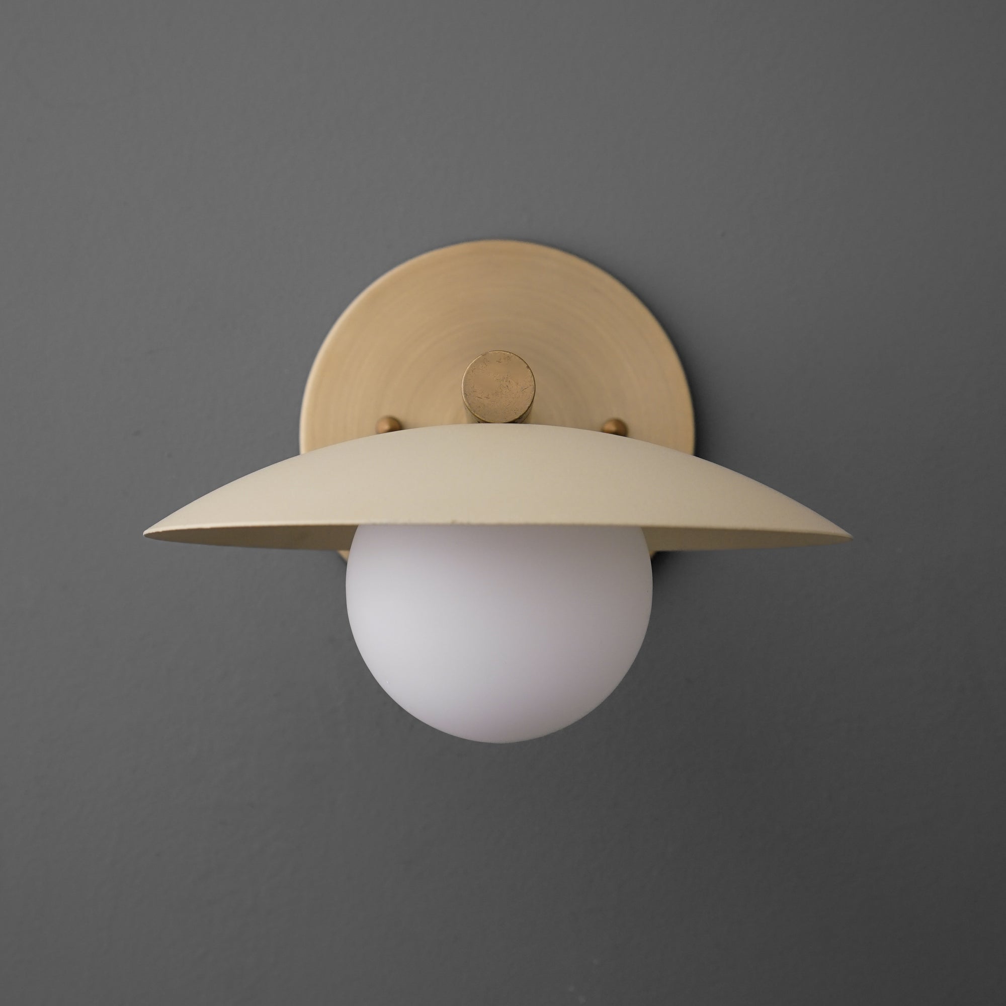 Minimalist wall sconce with antique brass finish and cream wide metal shade over white globe bulb. - SCONCE MODEL NO. 9875