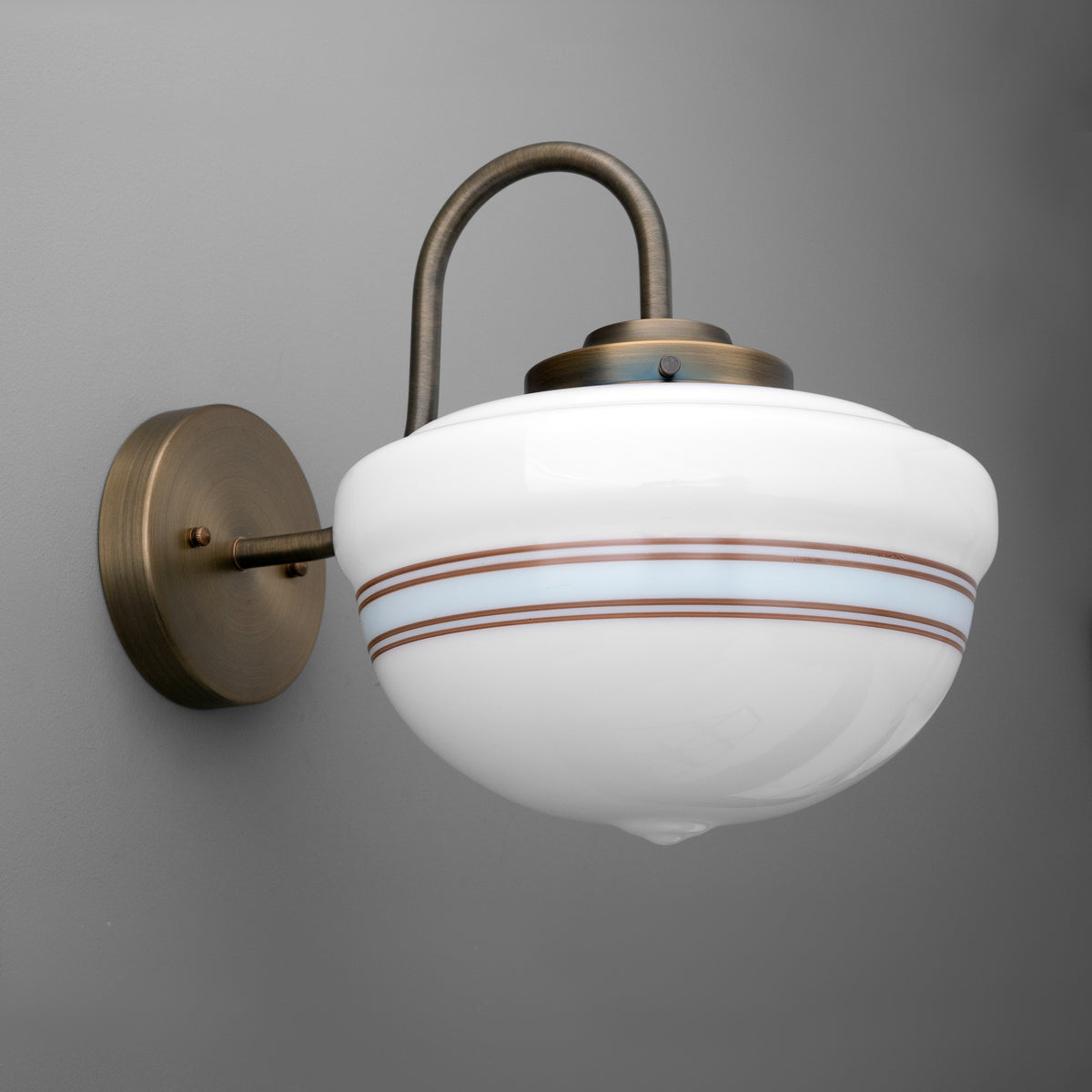 Single-light sconce in Antique Brass with a curved gooseneck arm holding an opal glass schoolhouse shade with a striped band, on a round wall plate. - SCONCE MODEL NO. 9156