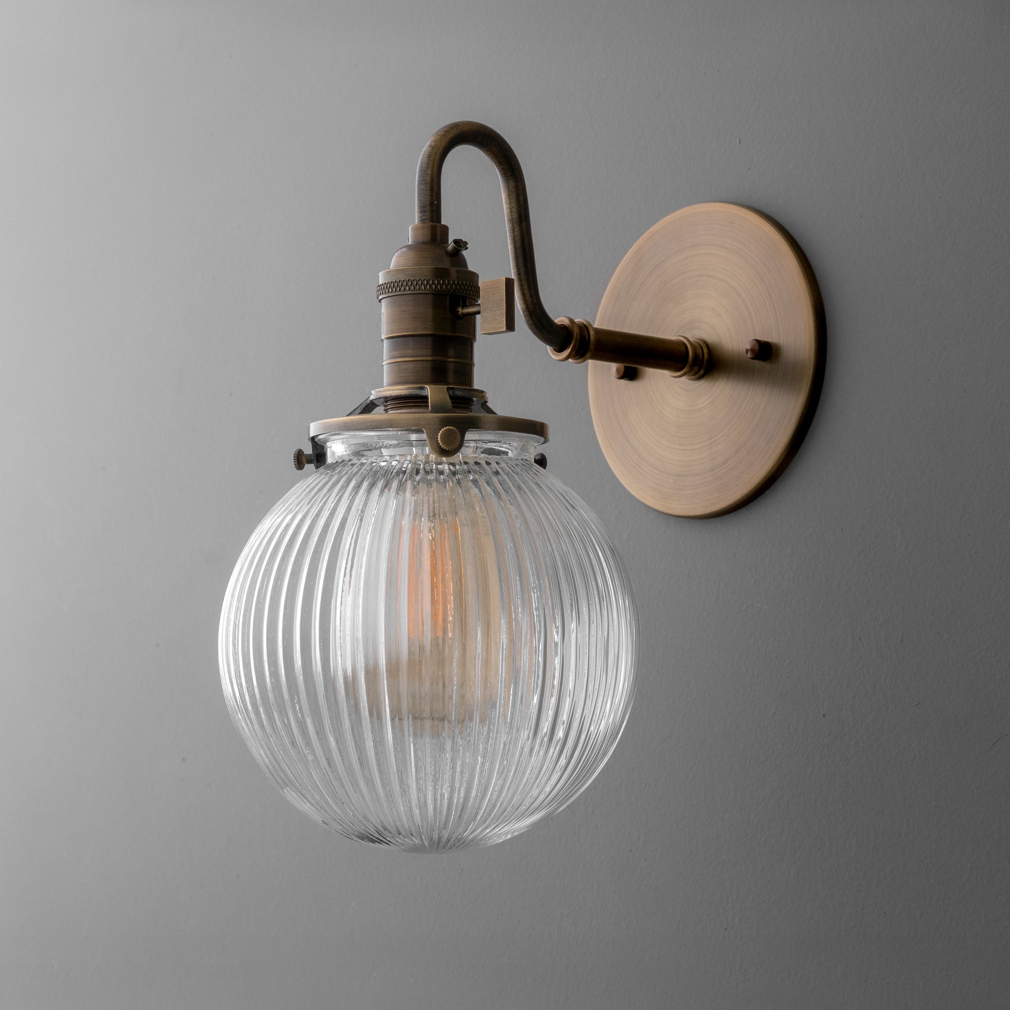 Antique brass wall sconce with ribbed clear glass globe shade and curved arm mounting. - SCONCE MODEL NO. 3331