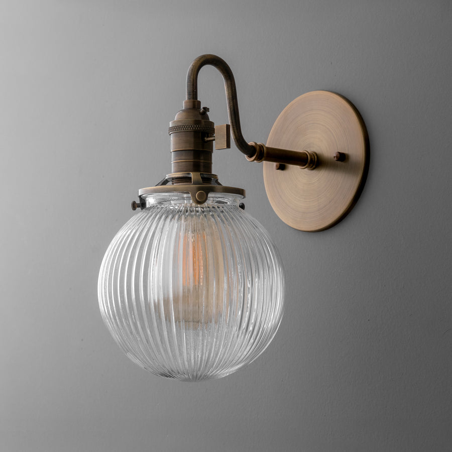 Antique brass wall sconce with ribbed clear glass globe shade and curved arm mounting. - SCONCE MODEL NO. 3331