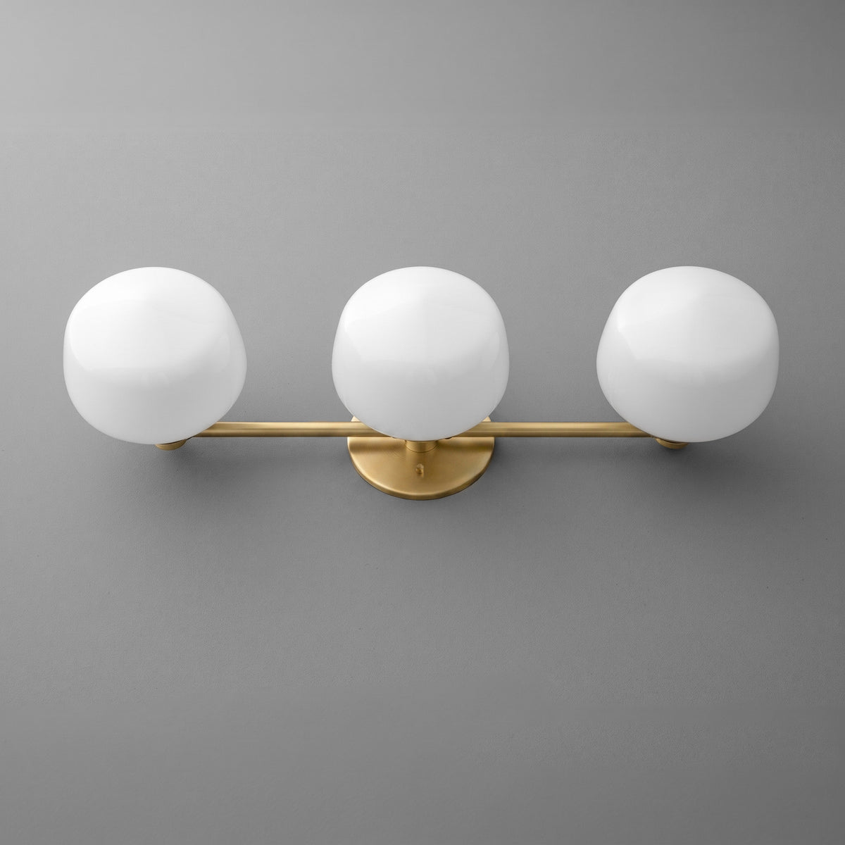 Modern vanity light with three white frosted globe bulbs and matte gold horizontal bar on gray wall. - VANITY LIGHT MODEL NO. 1106