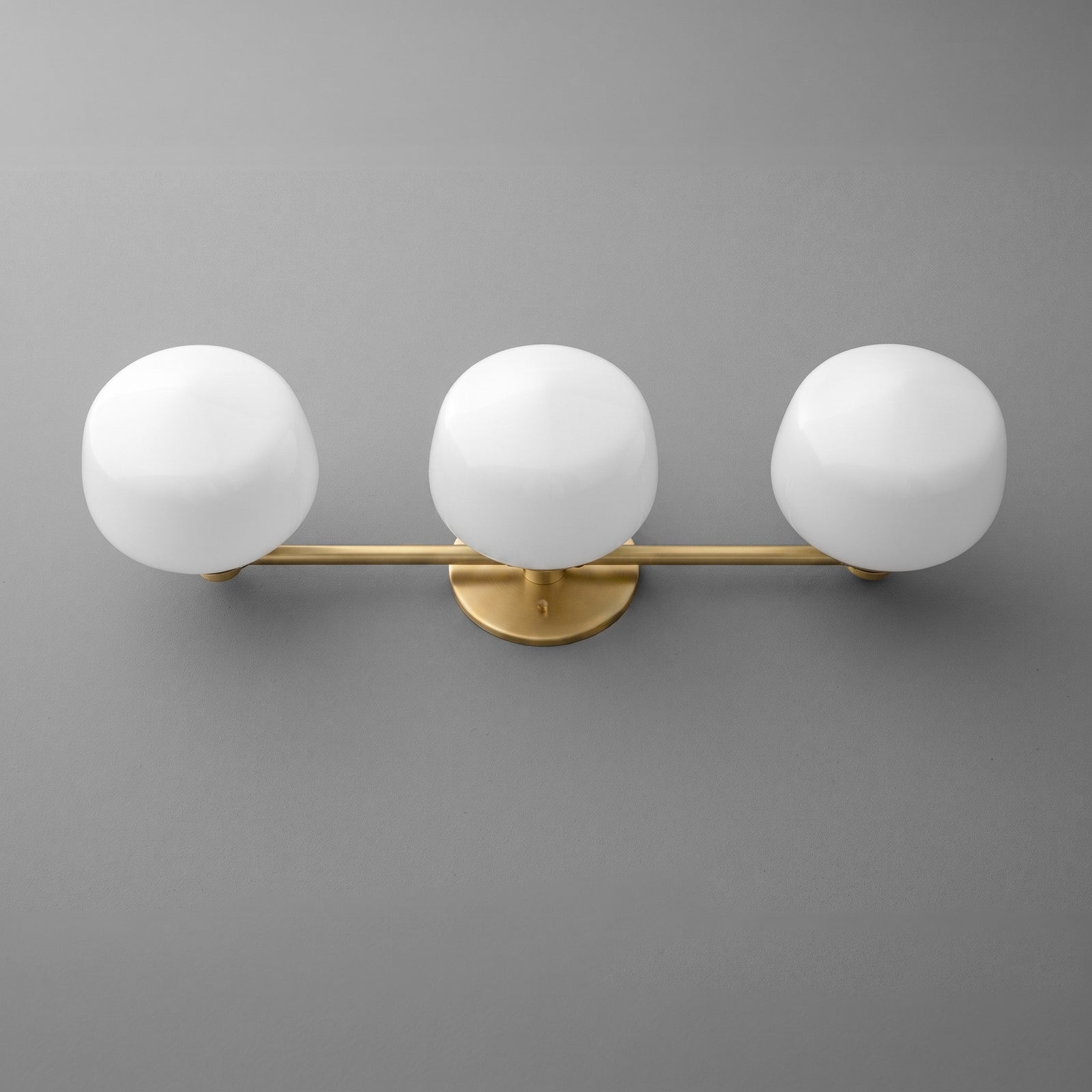 Modern vanity light with three white frosted globe bulbs and matte gold horizontal bar on gray wall. - VANITY LIGHT MODEL NO. 1106