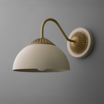 Raw brass wall sconce with curved arm and cream dome-shaped shade against gray wall. - SCONCE MODEL NO. 9408