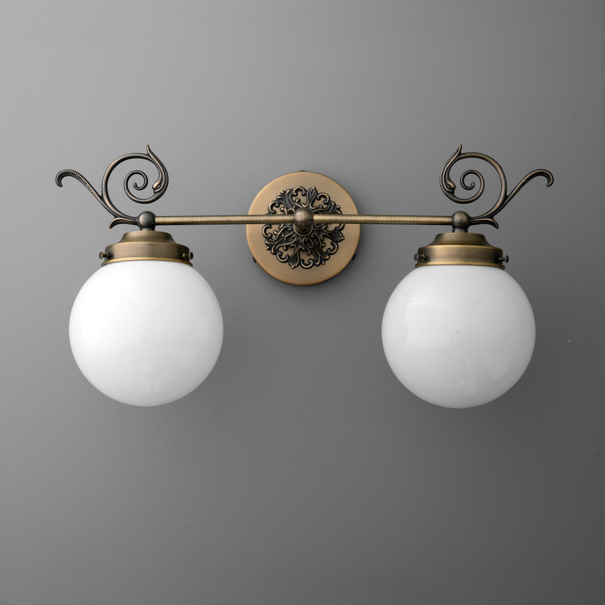 Antique brass vanity light with two frosted white glass globe shades and decorative scroll accents. - VANITY LIGHT MODEL NO. 1135
