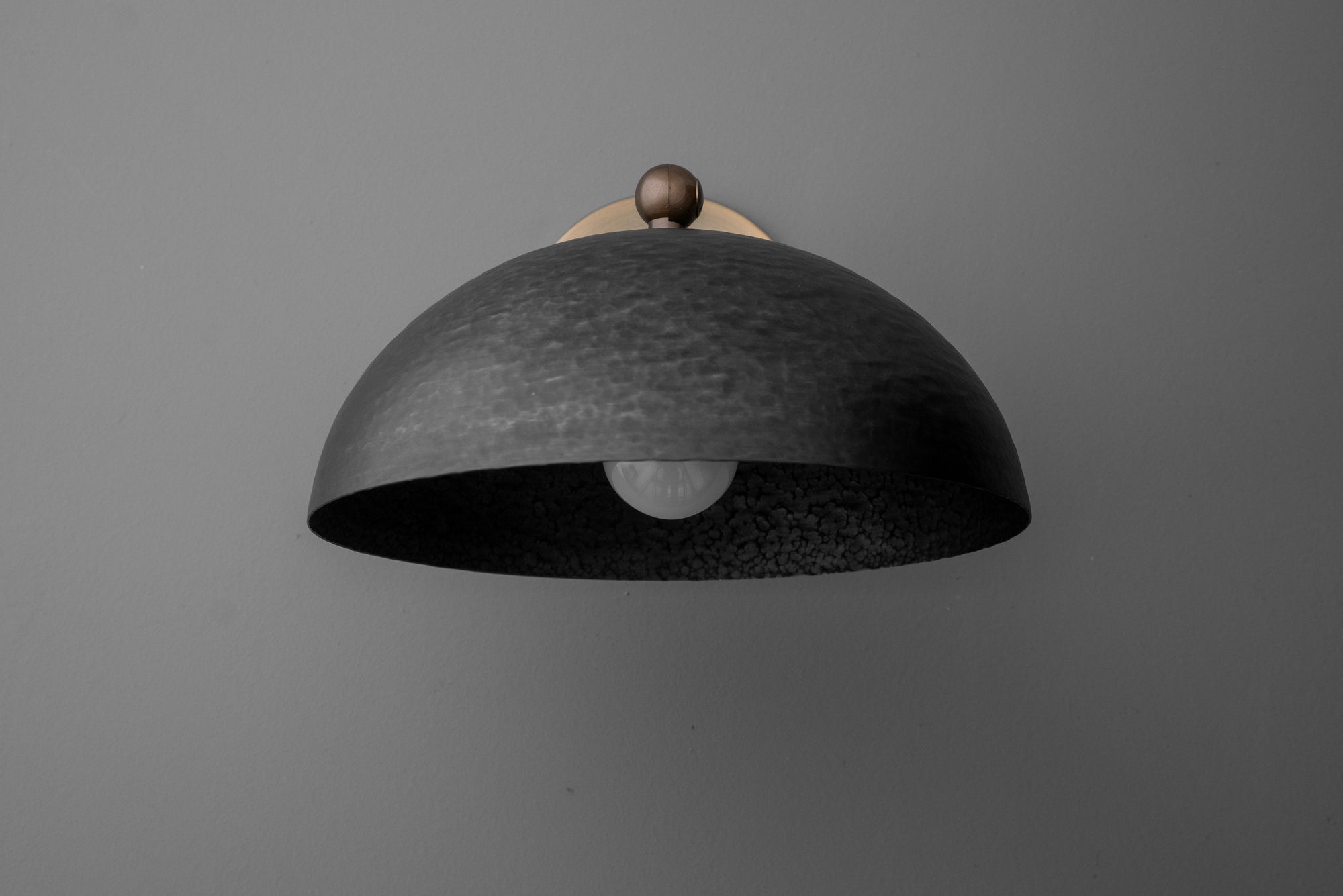 Black dome-shaped metal sconce with textured finish and small brass accent on top. - SCONCE MODEL NO. 3164