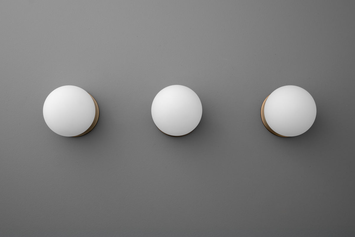 Three round white glass globe sconces with antique brass mounts on a gray wall. - Sconce Model No. 5206