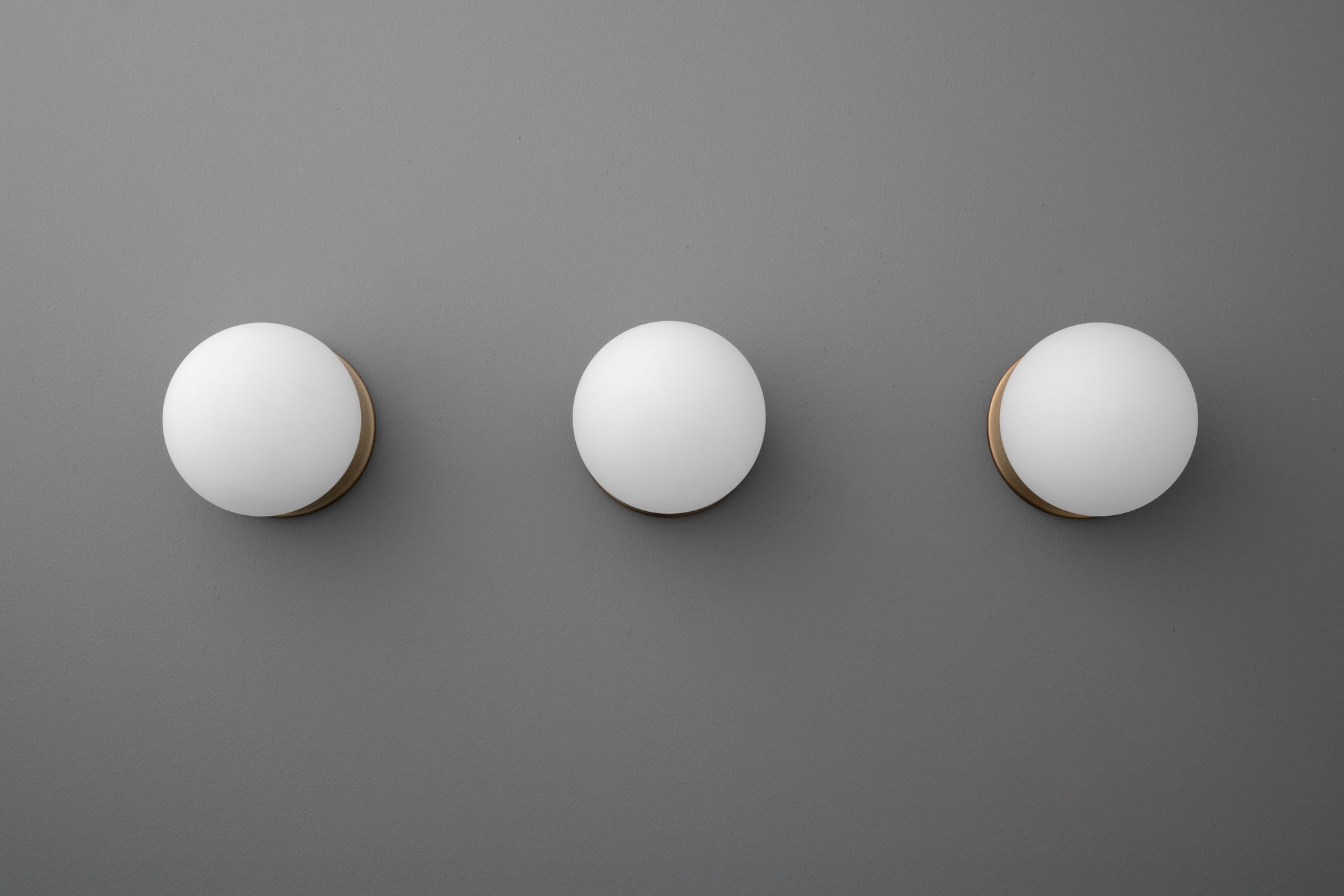 Three round white glass globe sconces with antique brass mounts on a gray wall. - Sconce Model No. 5206